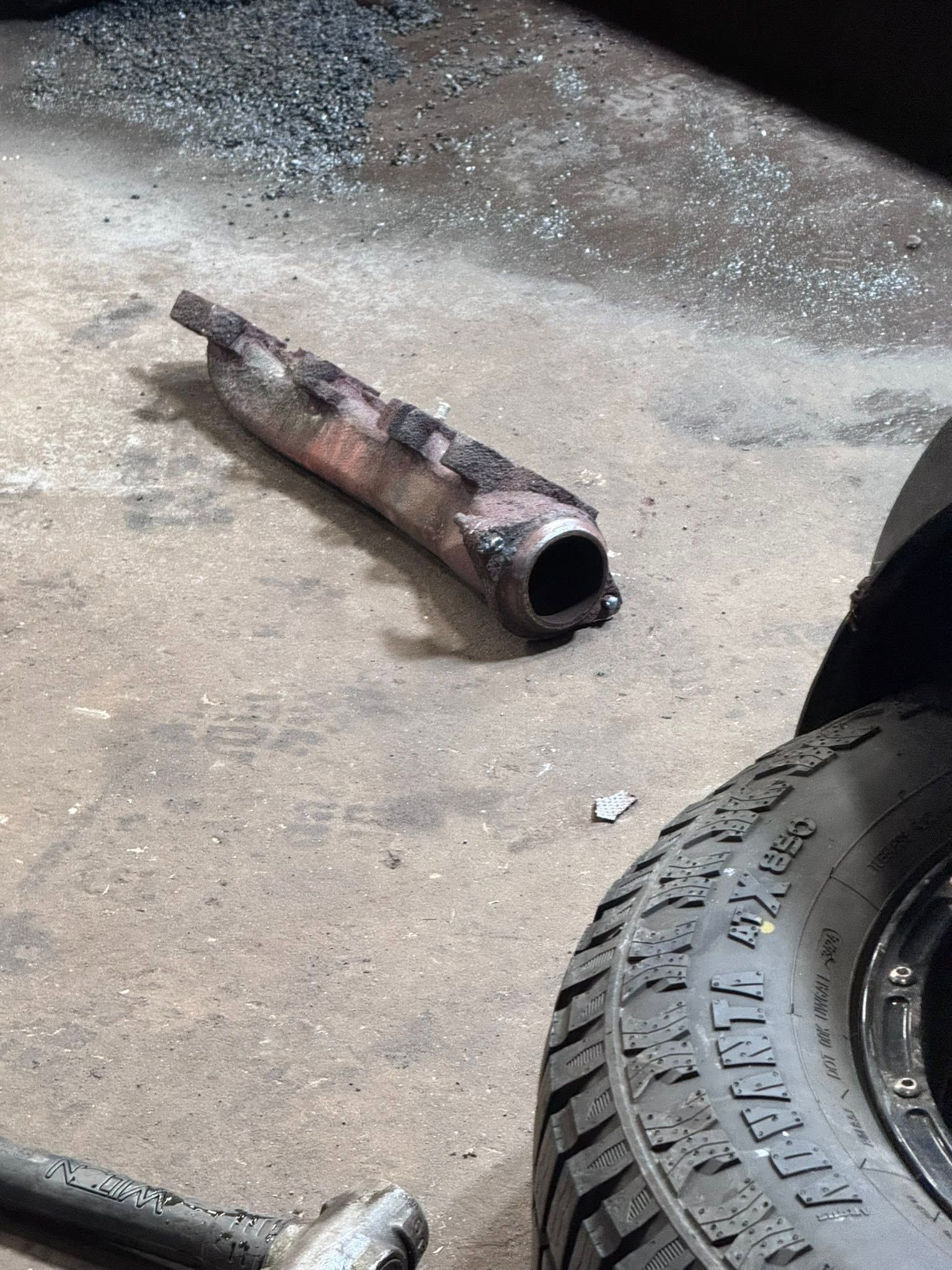 Rusty exhaust pipe lying on concrete floor beside a car tire.