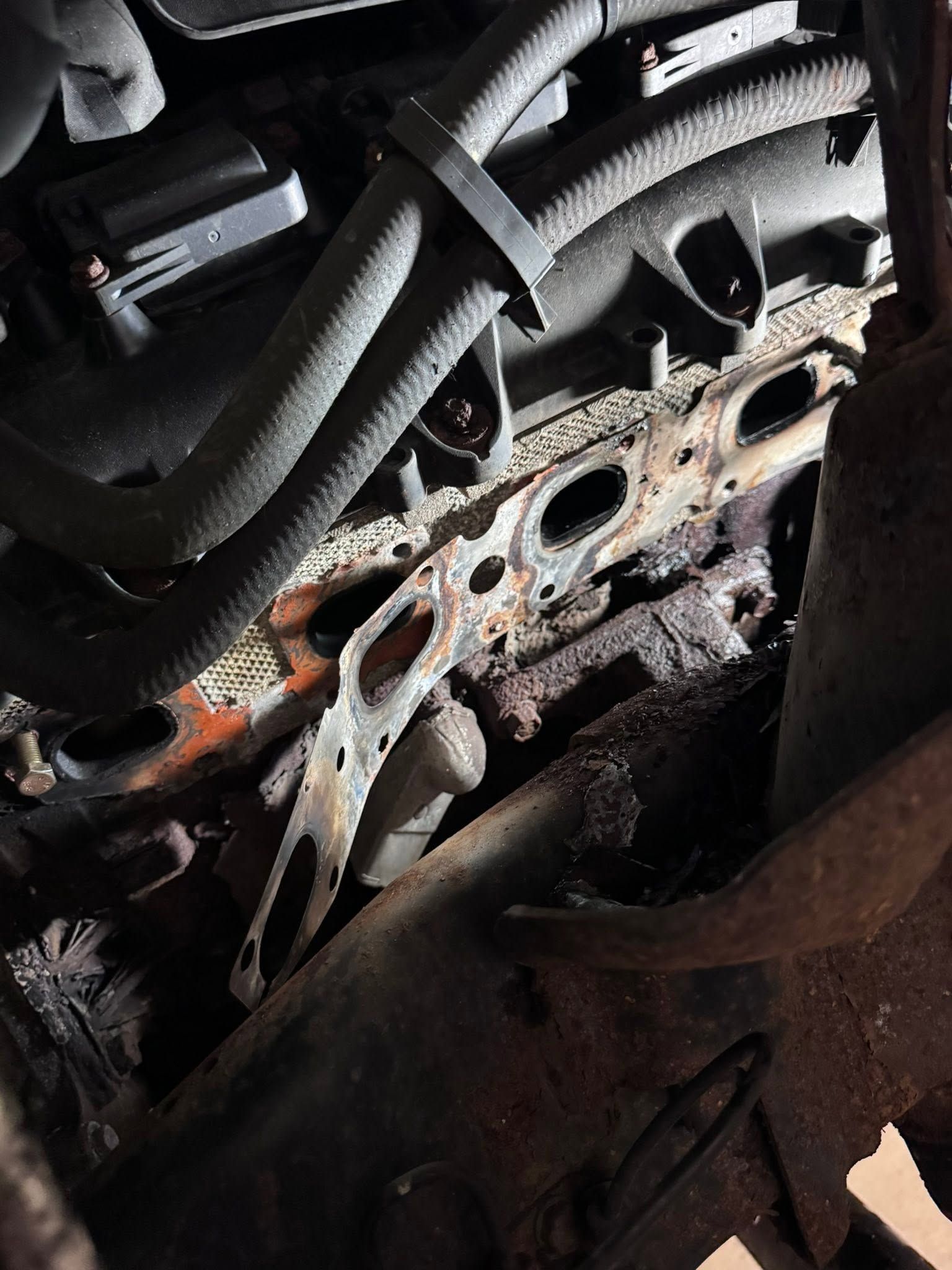 Rusty engine block and metal tubing inside a damaged car engine bay.