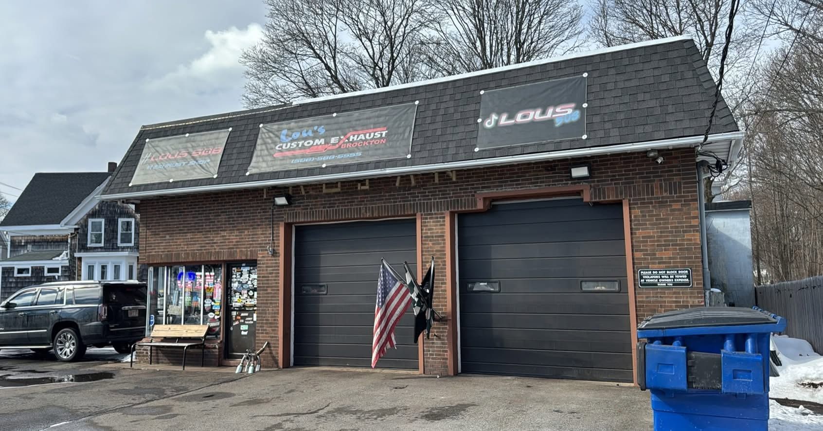 Exterior of a rustic building with two garage doors, American flag, parked truck, and blue dumpster.