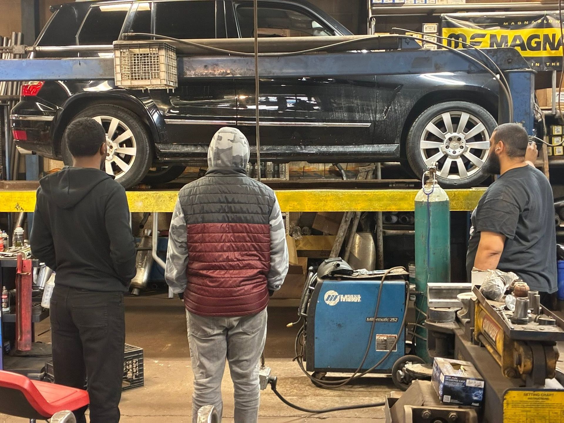 Black SUV on a lift in an auto repair shop with three people standing nearby
