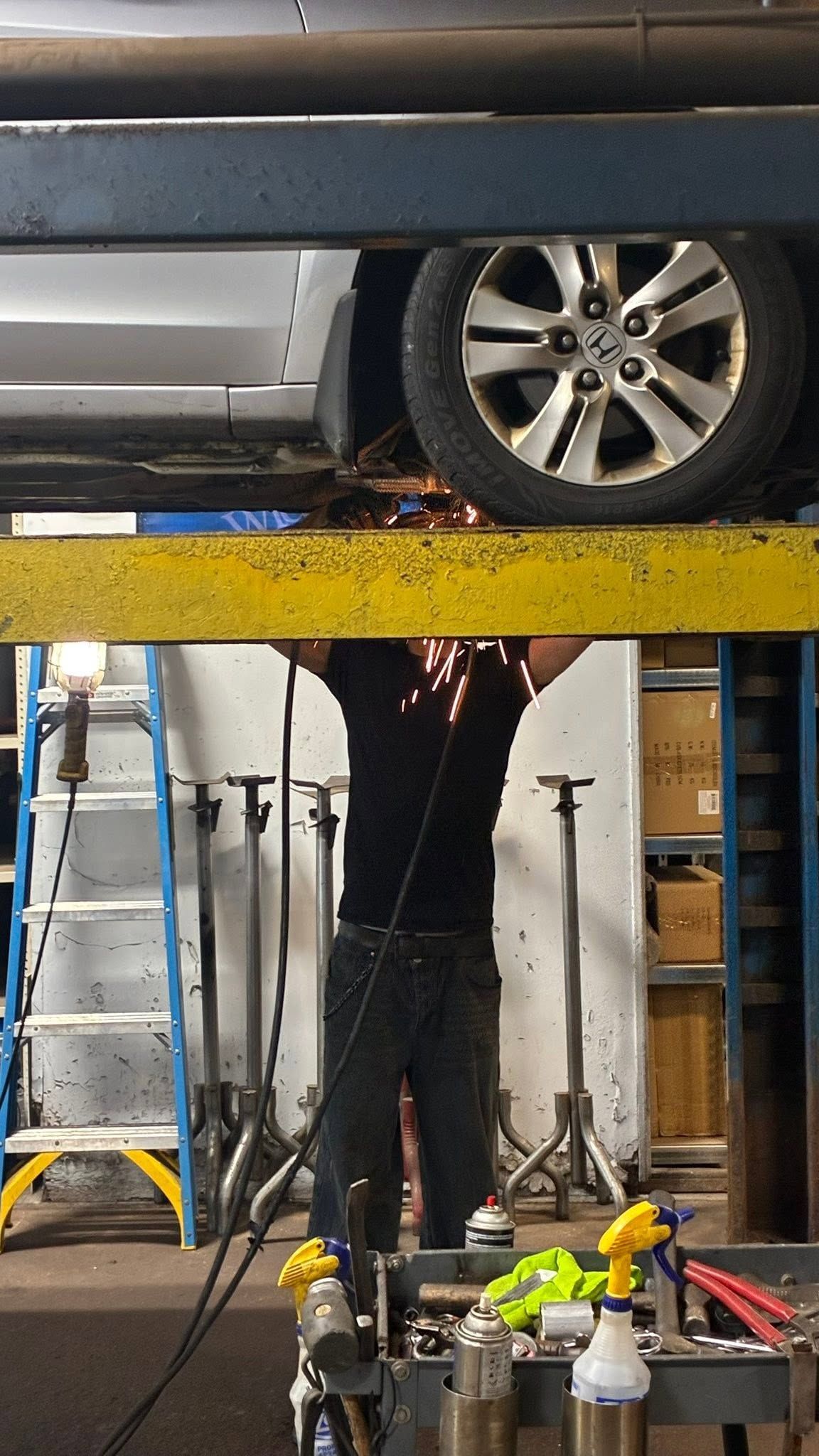 Car on a lift in an auto shop, with a person working below and tools in the foreground