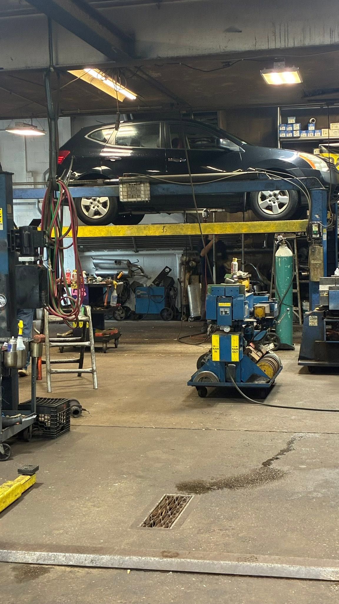 Blue car on a hydraulic lift in an auto repair shop, with tools and equipment around it.