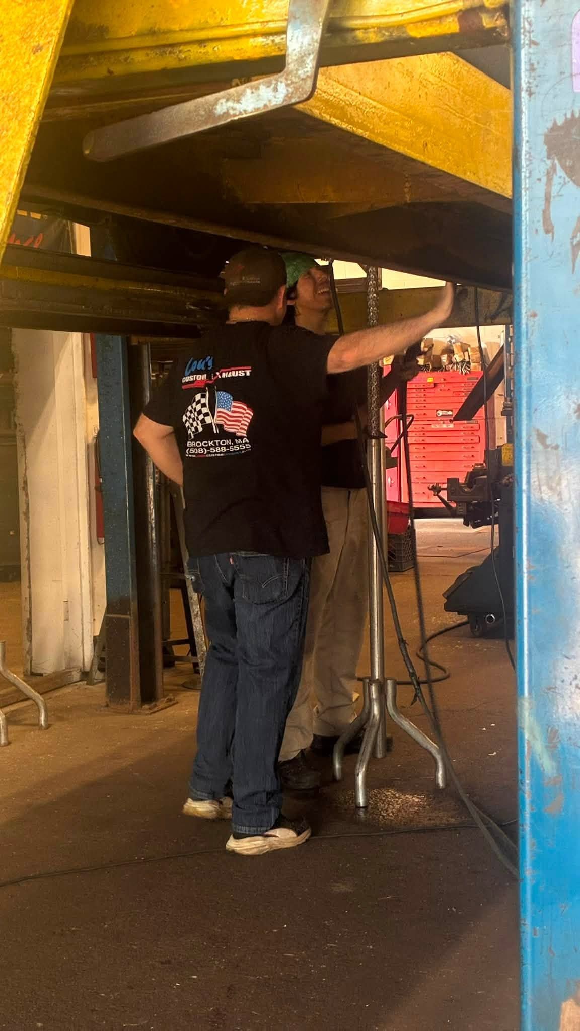 Person standing under a vehicle in a garage, using a tool near the underside of the car.