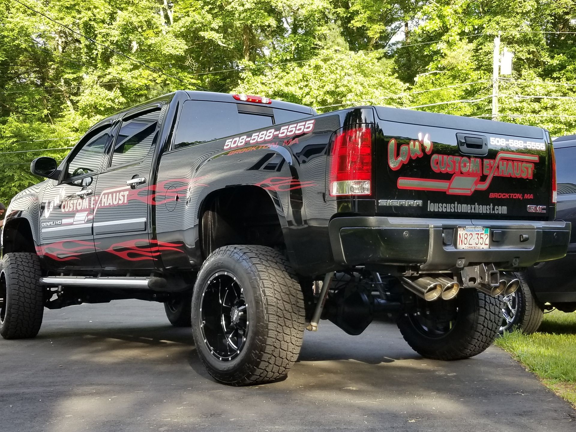 Black lifted pickup truck with red decals parked on a road beside green trees