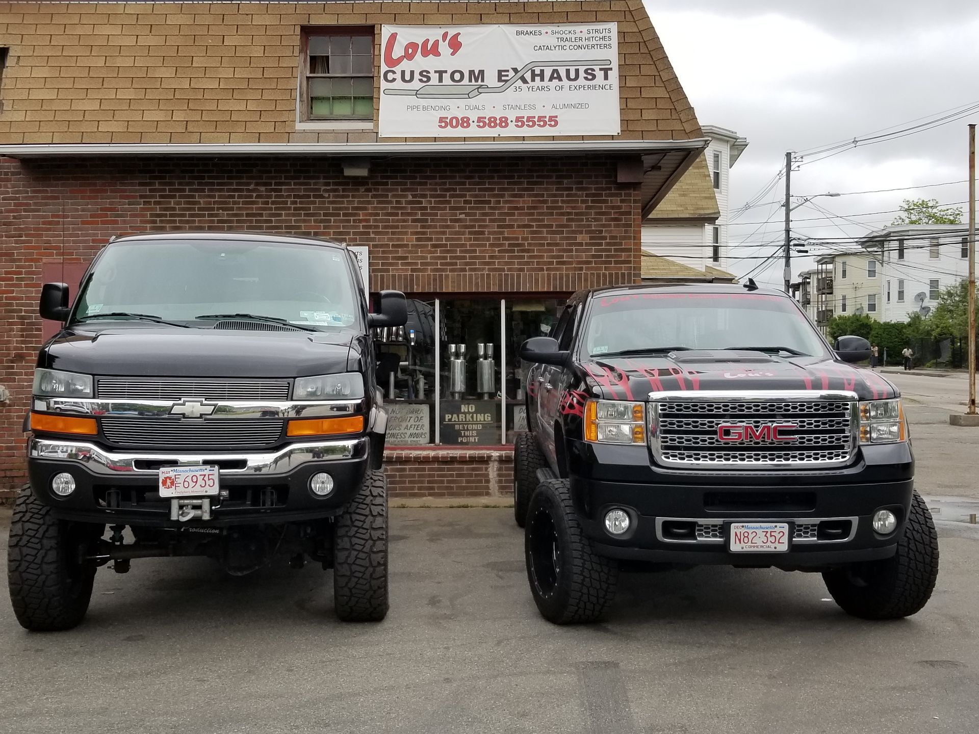 Two lifted black pickup trucks parked in front of a custom exhaust shop