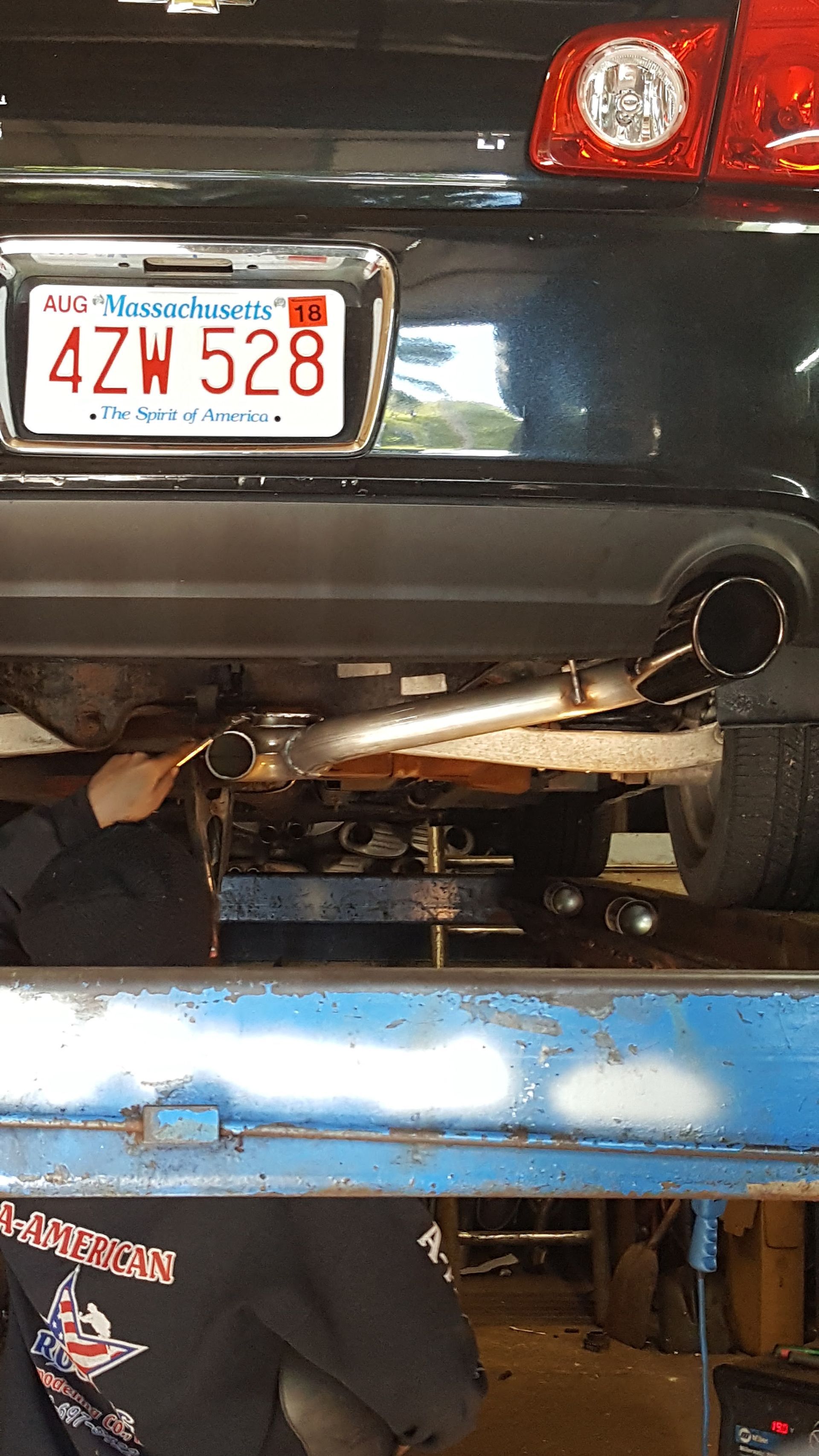 Rear of a black car lifted on a blue hydraulic jack, with a New Hampshire license plate visible.