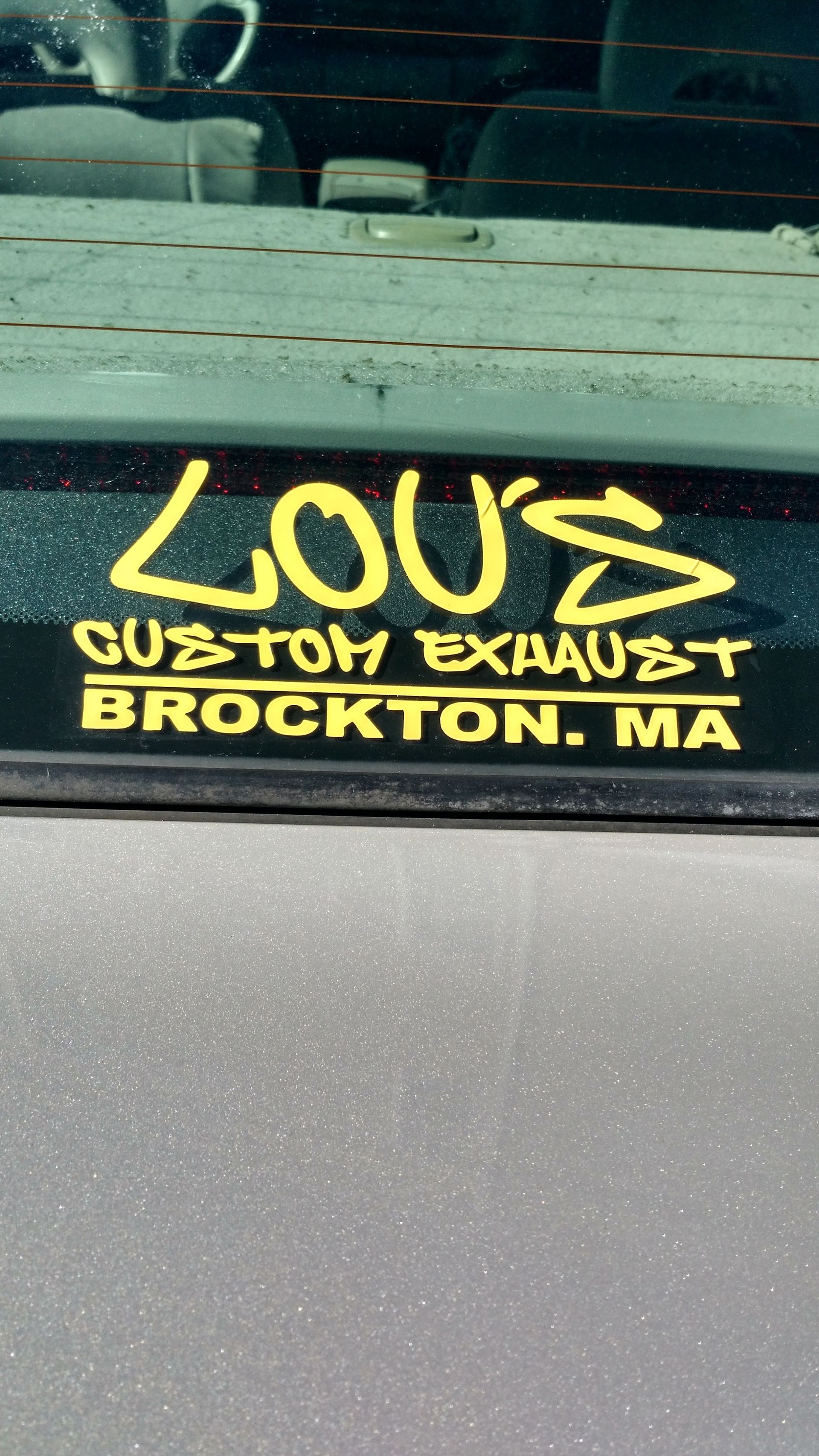 Yellow “LOUIS” and “CUSTOM EXHAUST” sticker with “BROCKTON, MA” on a car window.