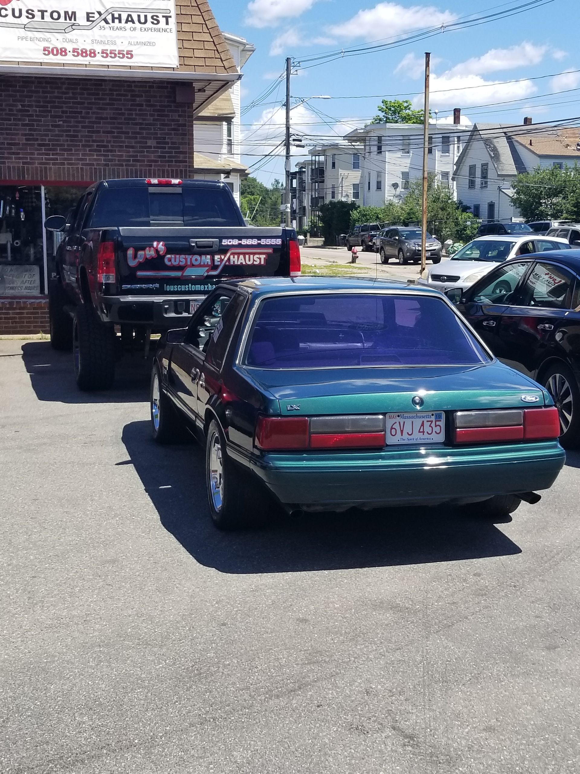 Teal car towing a black truck on a sunny city street