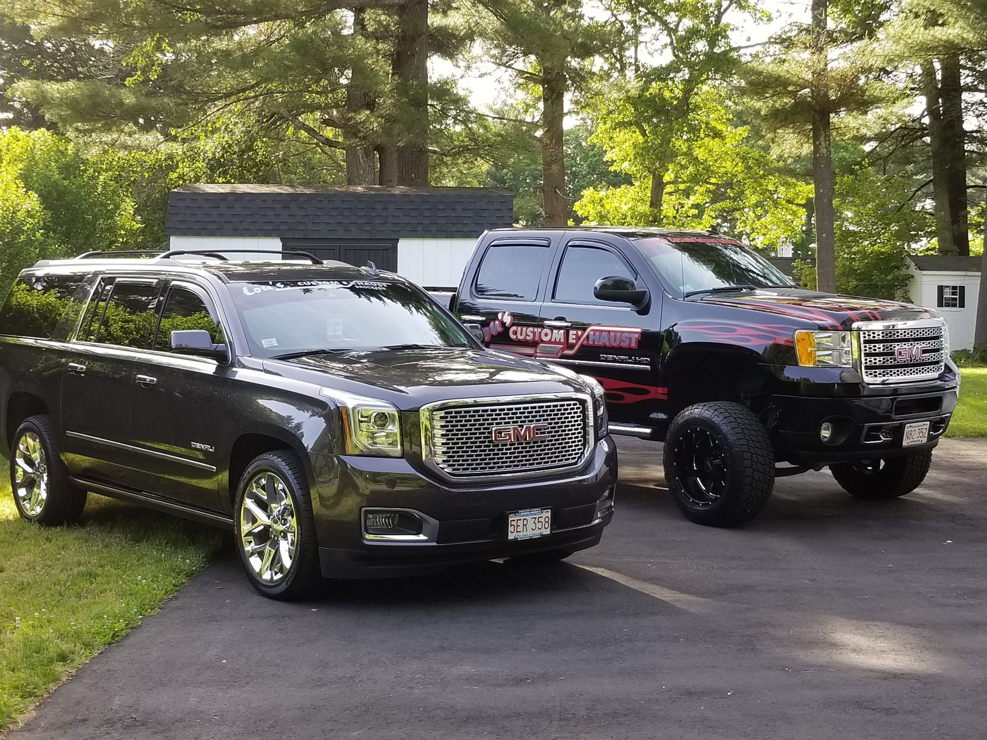 Two large SUVs parked on a driveway beside a grassy, wooded area.