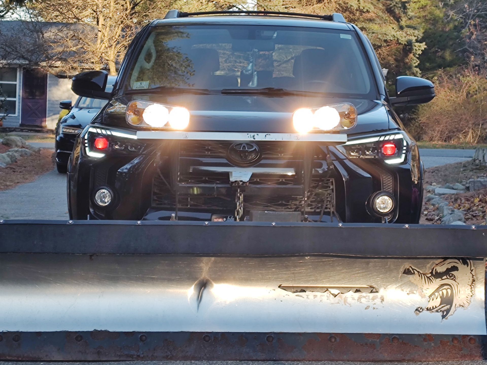 Black Toyota SUV with bright headlights behind a damaged metal barrier outdoors