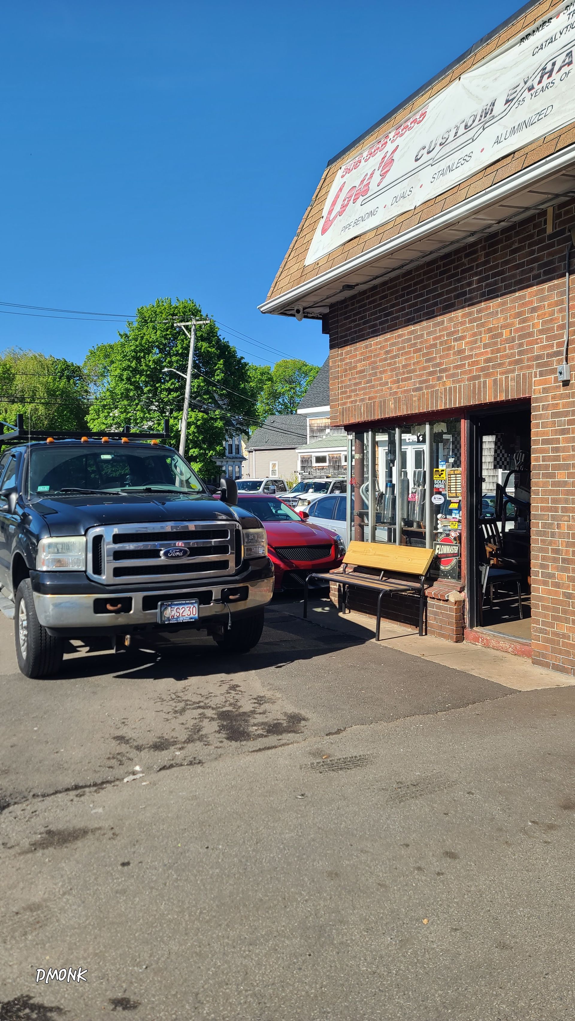 Parked pickup truck and red car beside a brick storefront on a sunny street