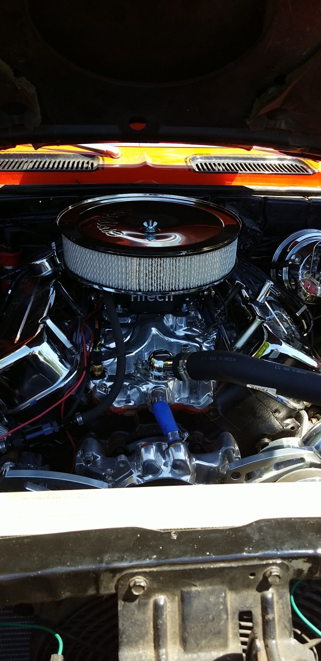 Car engine bay with chrome air filter and orange support bar at the rear.