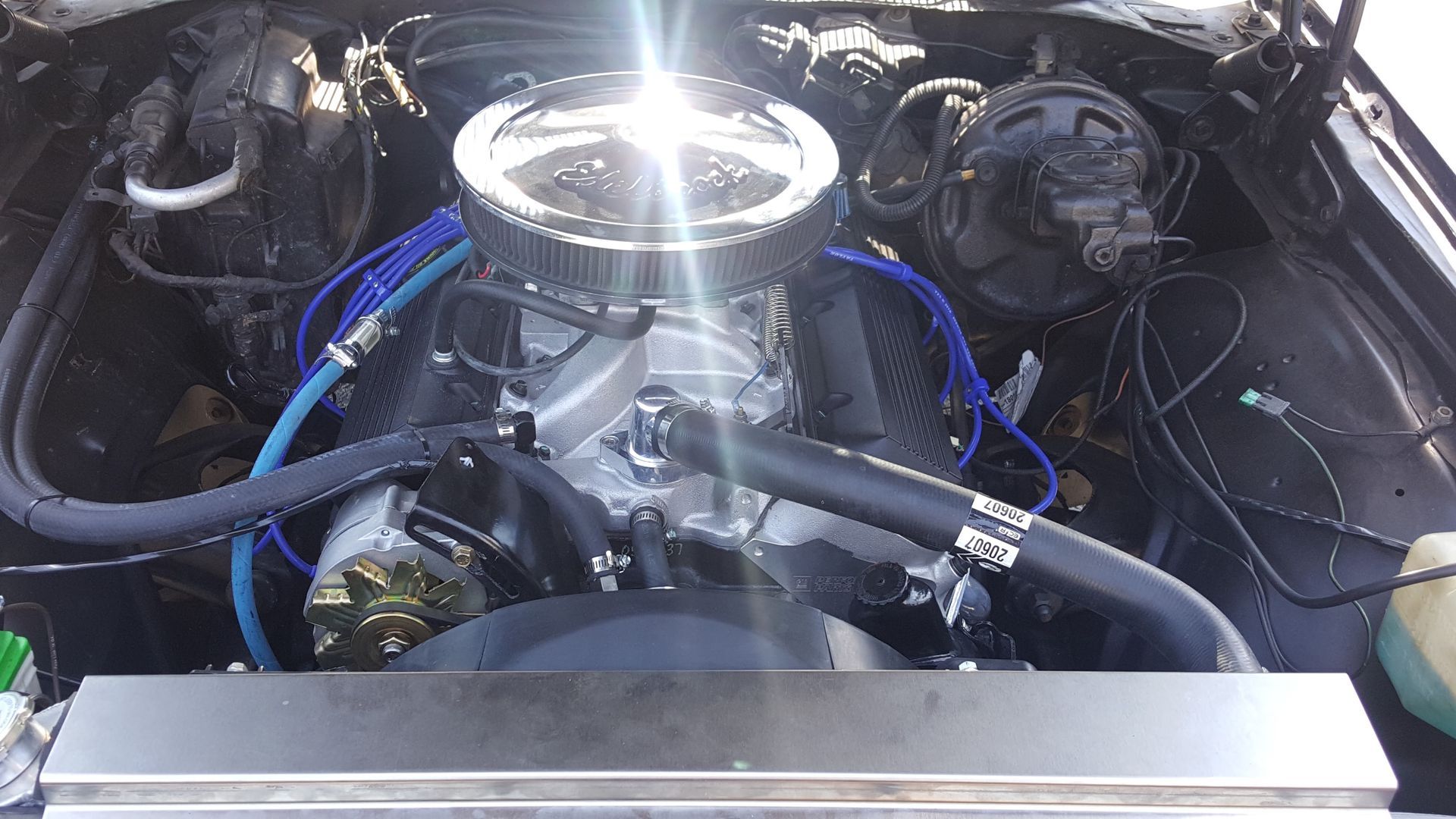 Car engine bay with chrome air cleaner, blue hoses, and polished components.