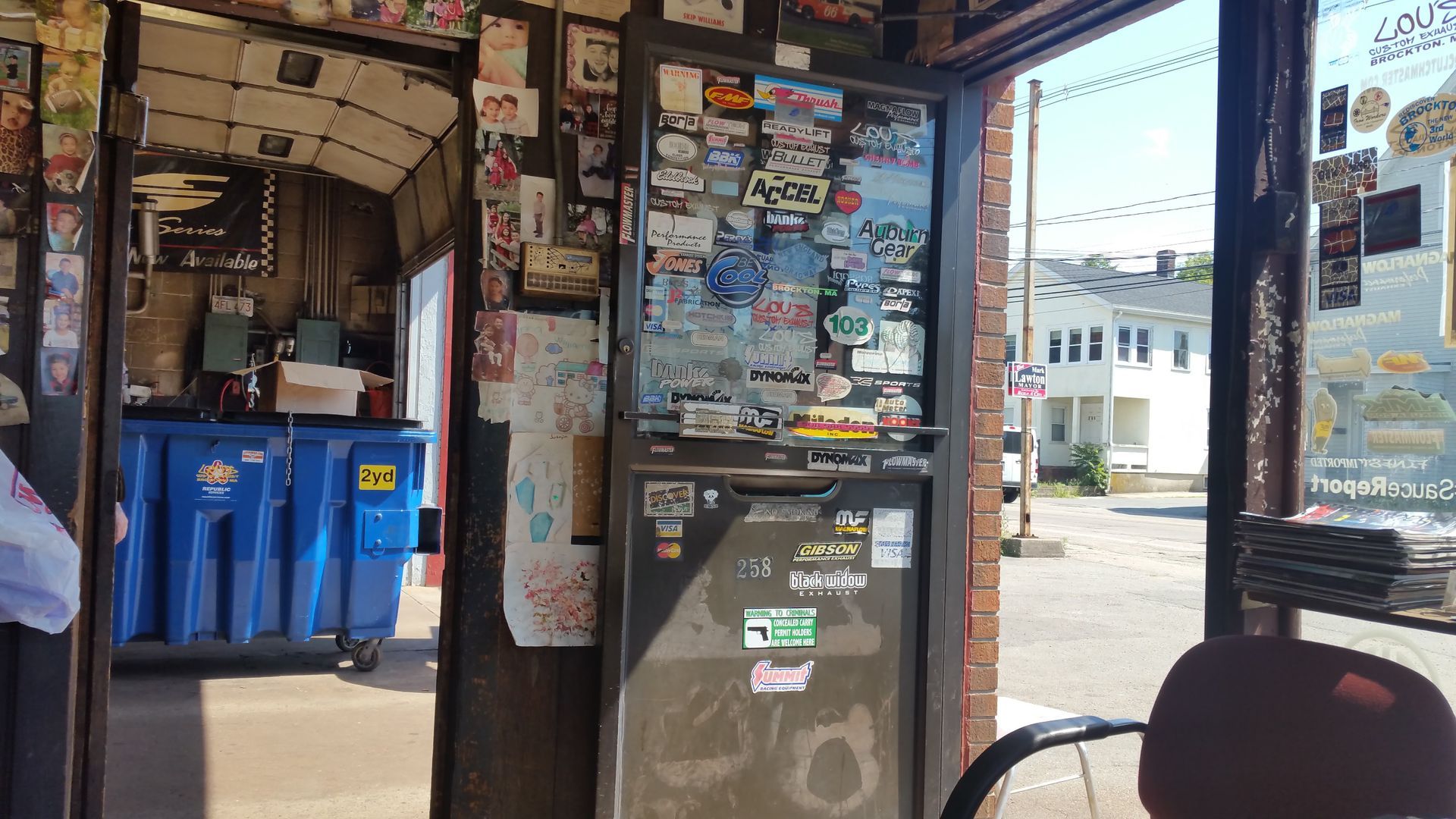 Interior of a sticker-covered bus or trolley, with blue trash bins and an open door to the street.