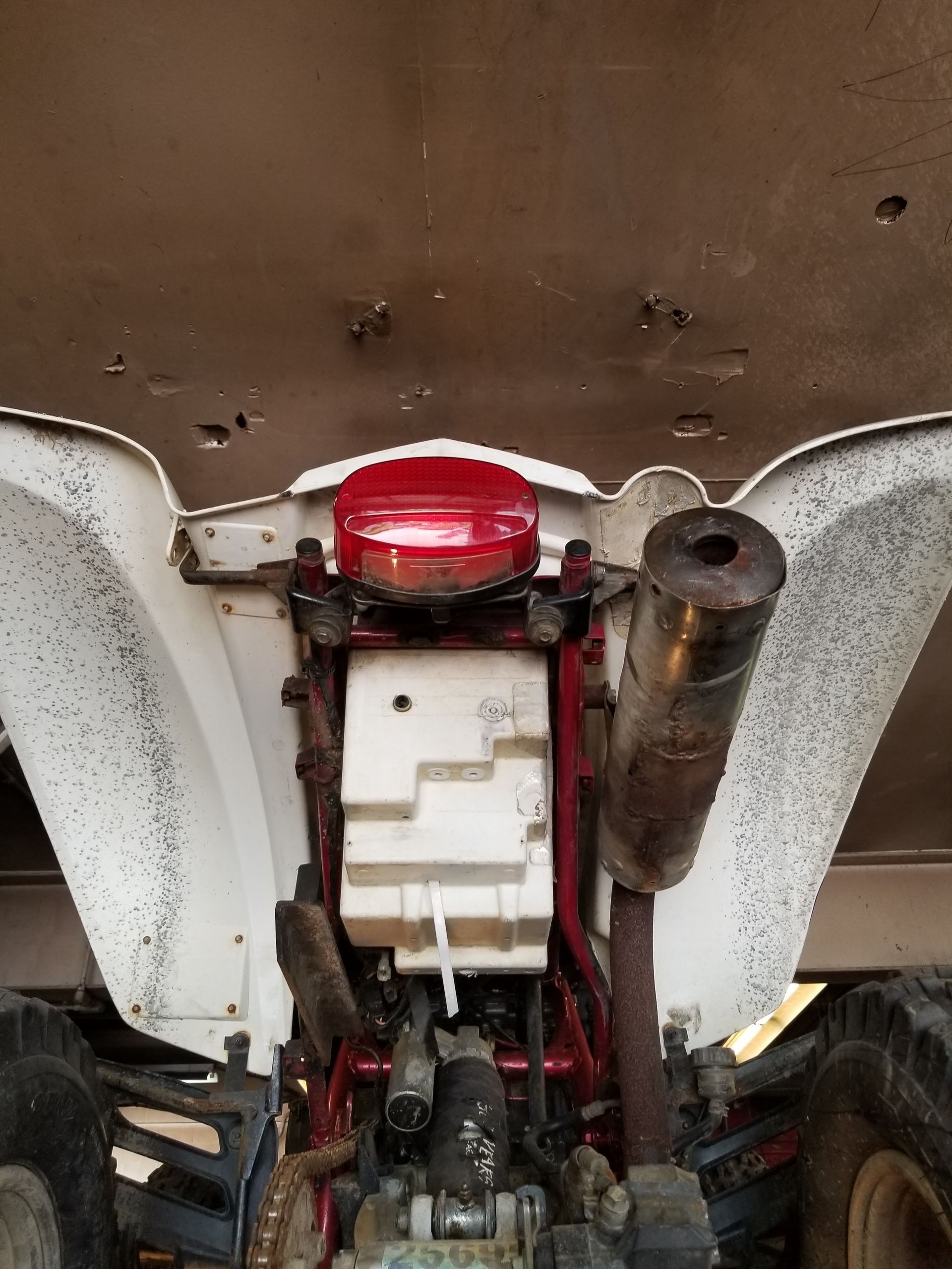 Underbody view of a red and white machine engine with rusted parts and a muffler