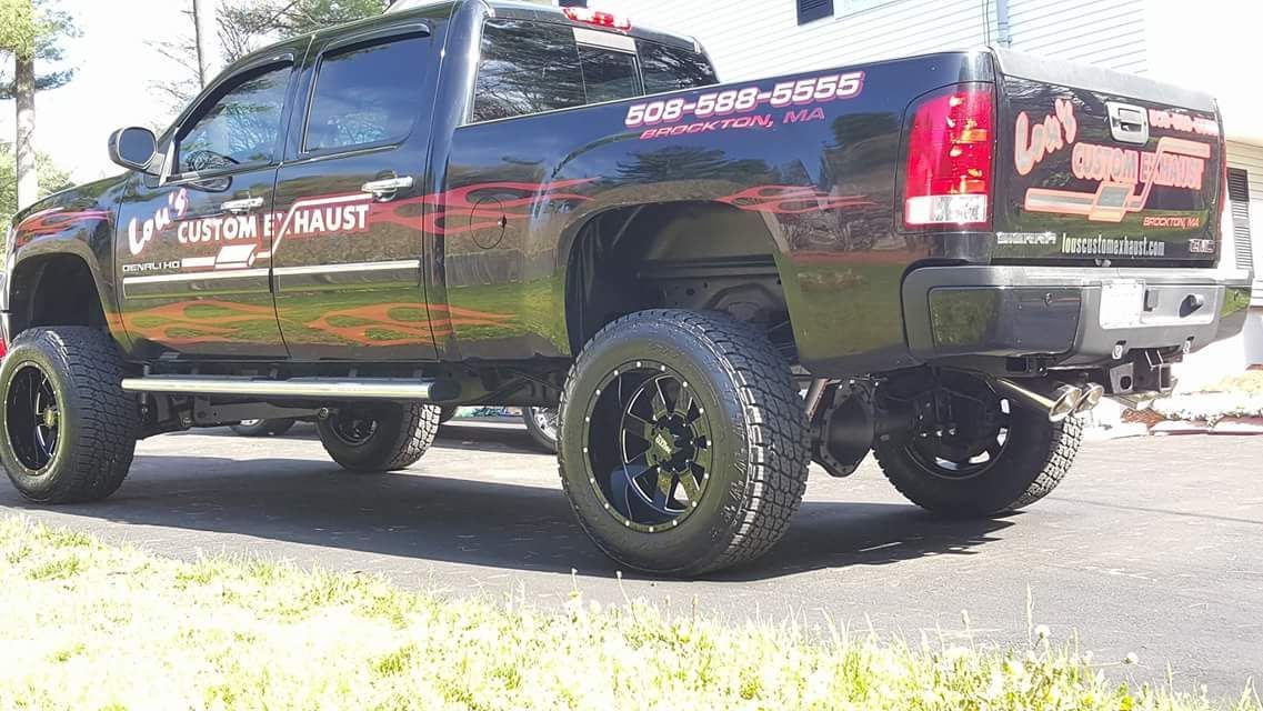 Lifted black pickup truck with custom graphics, parked outdoors on grass in bright sunlight.