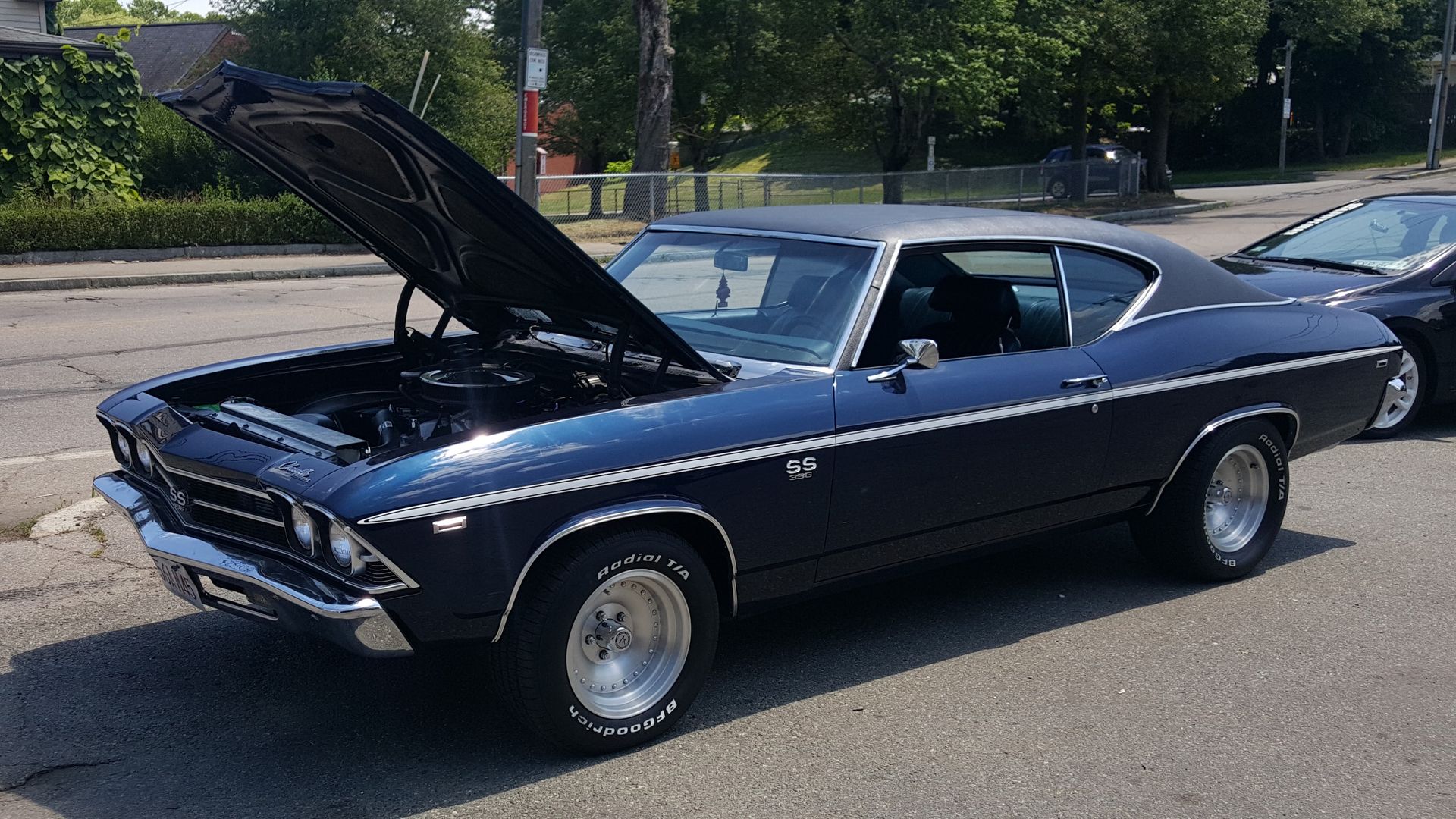 Black classic car with hood open, parked outdoors on a sunny street.