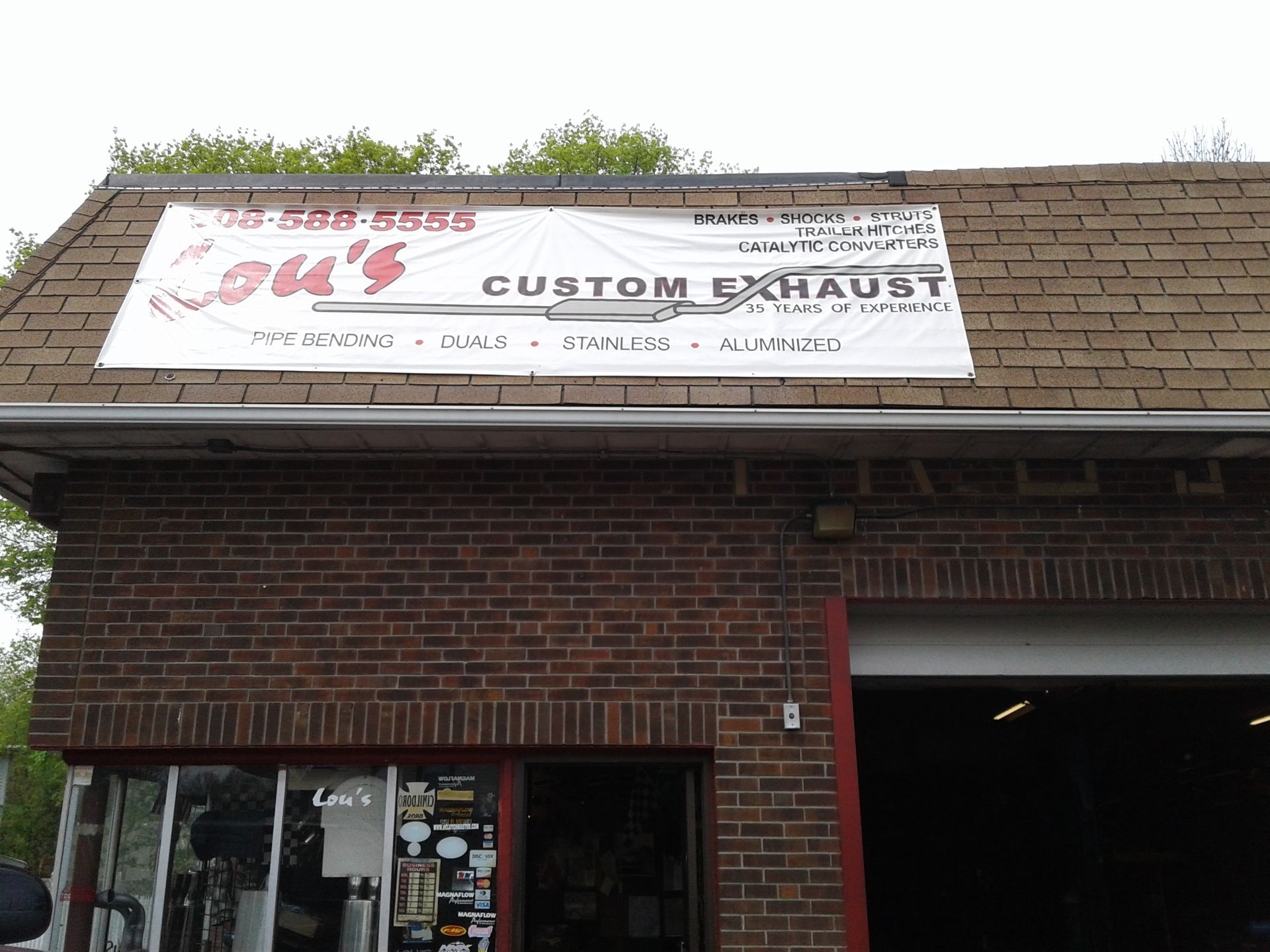 Brick storefront with a white “Custom Exhaust” sign above a shop entrance and open garage bay.