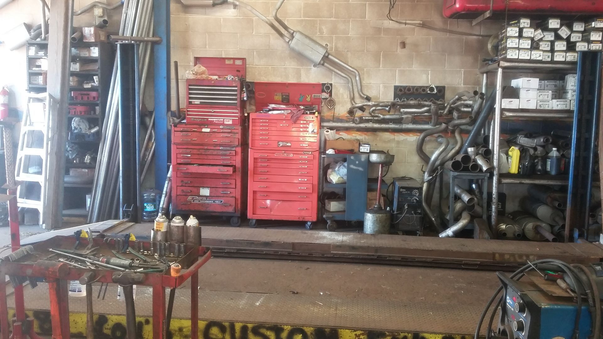 Cluttered auto repair shop with red tool cabinets, a workbench, and car parts on shelves