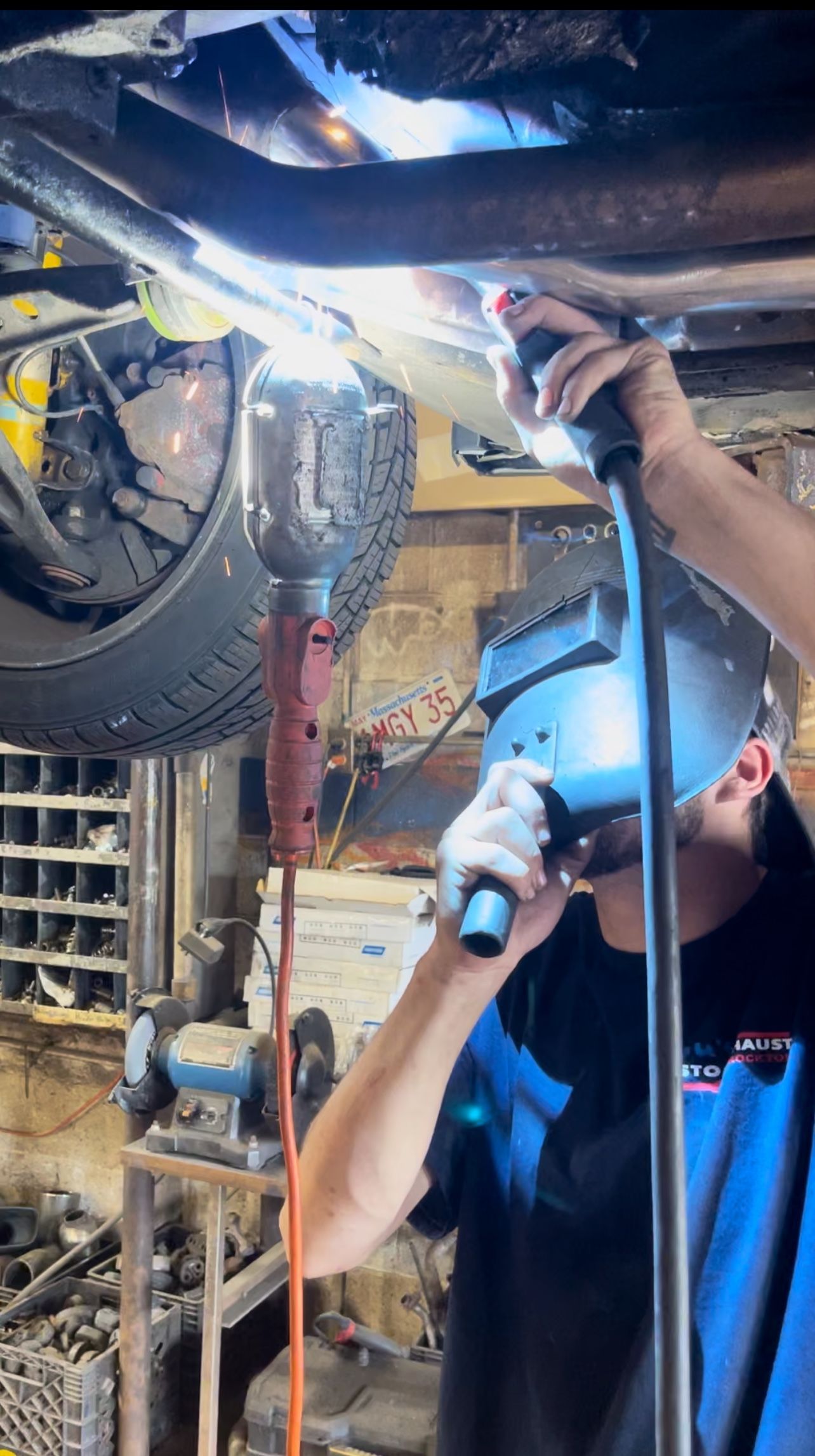 Technician using a flashlight to inspect machinery under a vehicle in a workshop