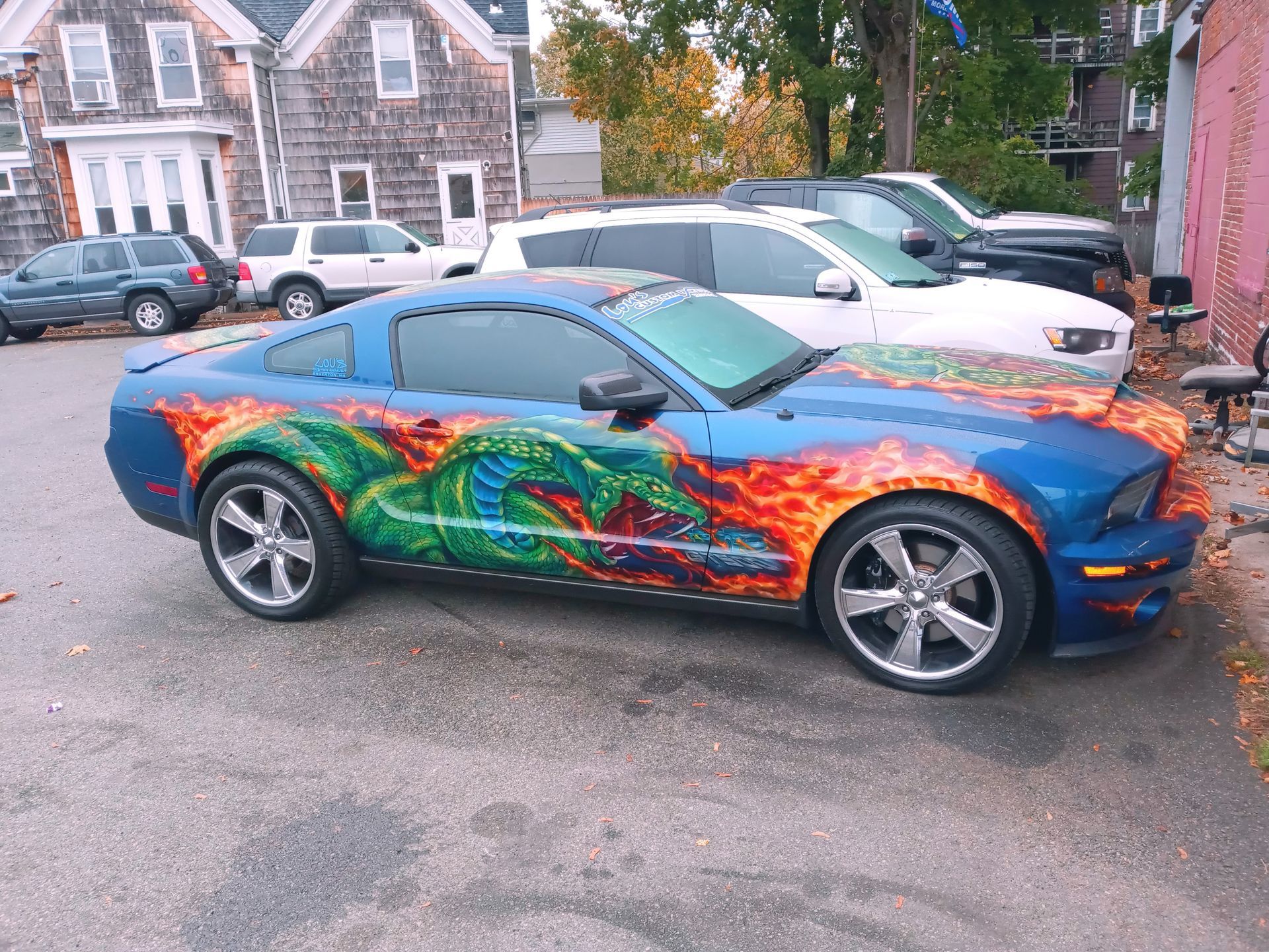 Blue sports car with colorful dragon wrap parked in a residential driveway