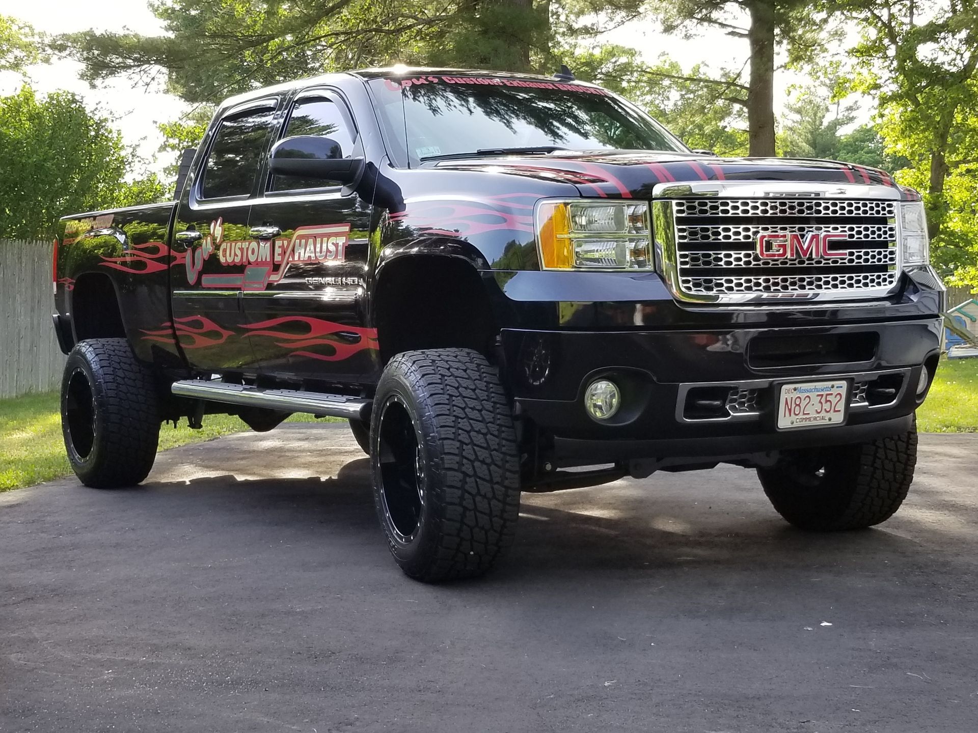 Lifted black pickup truck with chrome grille and oversized tires parked outdoors on a driveway.