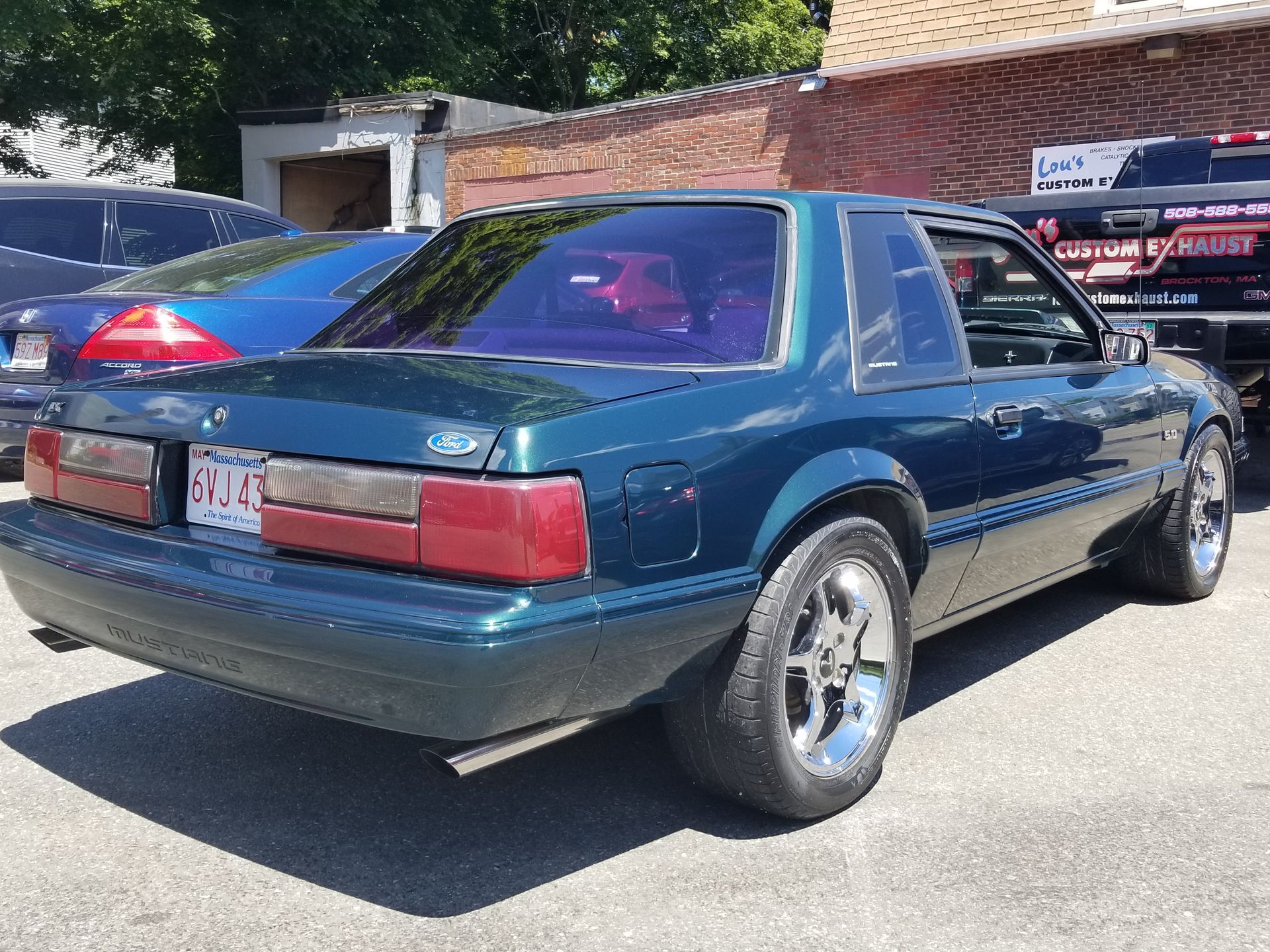 Dark green classic coupe parked on a street, rear three-quarter view.