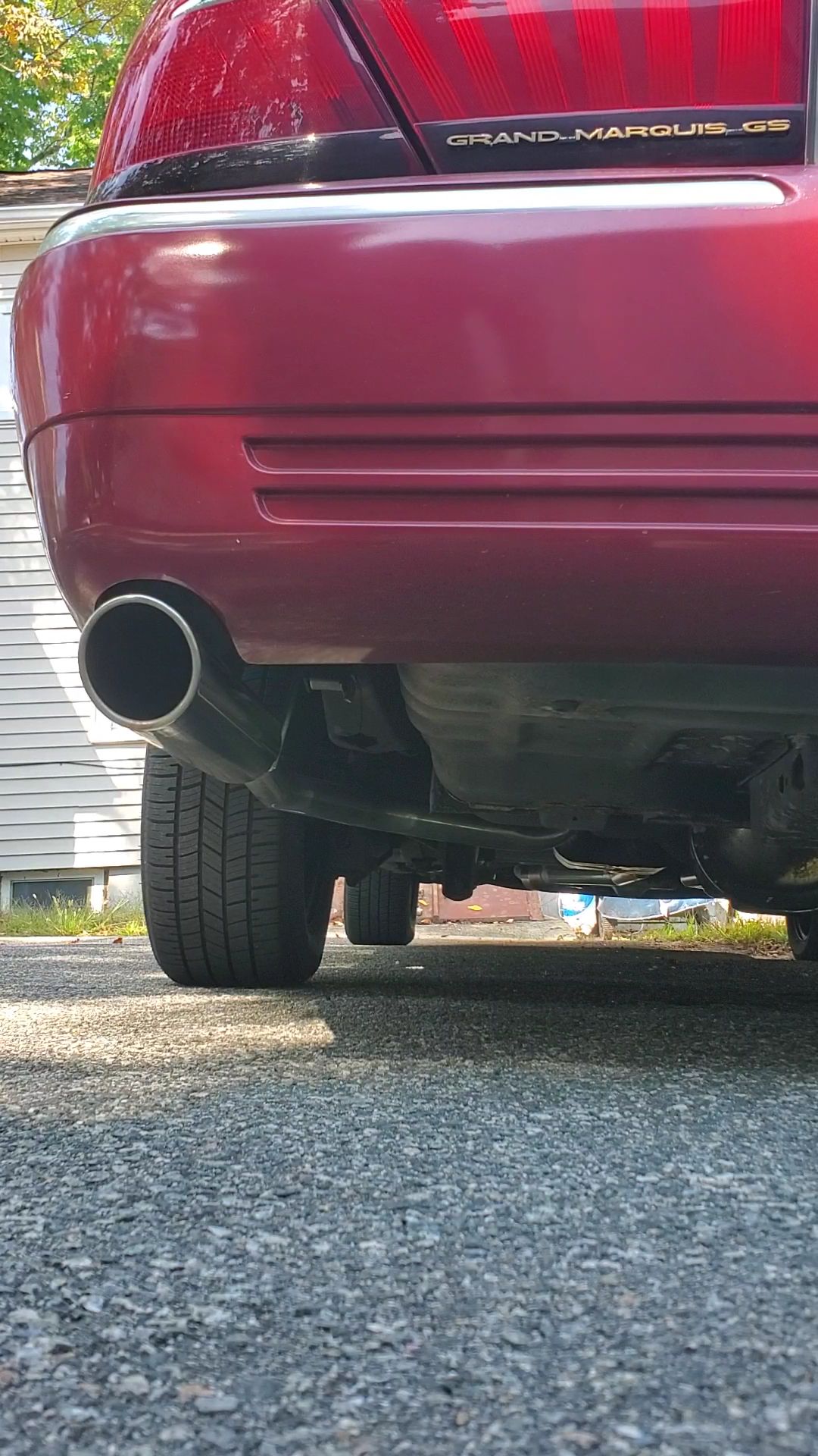 Rear of a red car with a large exhaust pipe, parked on a gravel driveway.