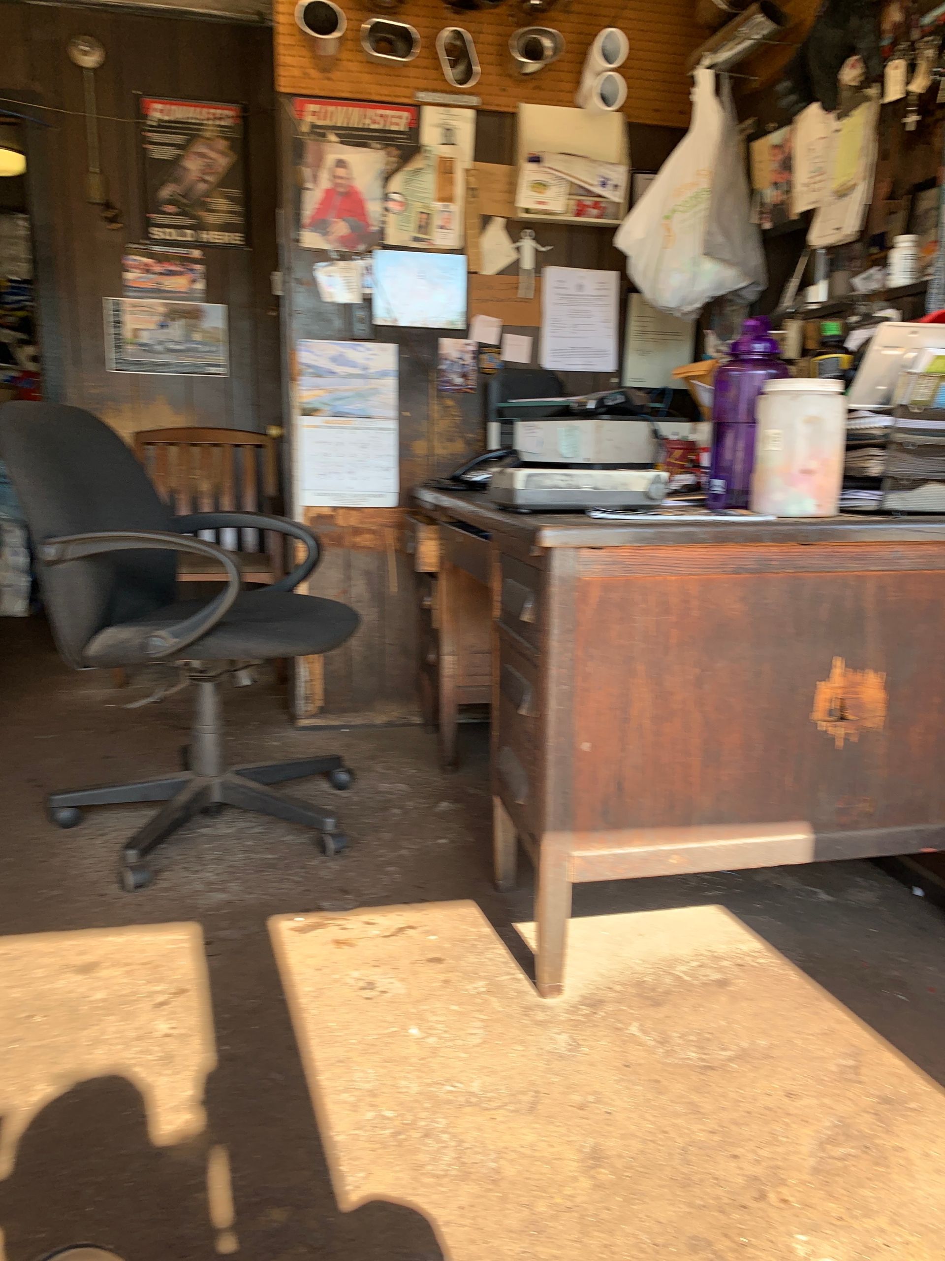 Cluttered office with a desk, rolling chair, and papers inside a rustic wooden room