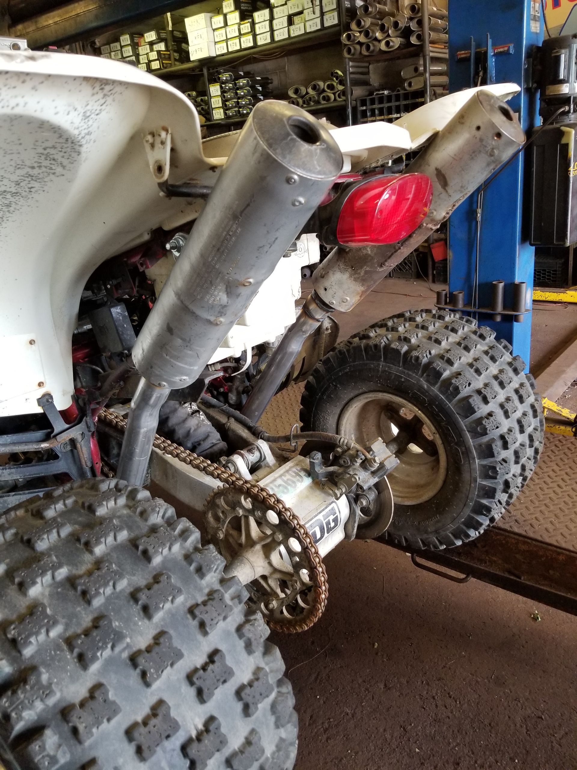 Close-up of a quad bike’s rear wheel, exhaust, and red taillight in a garage.