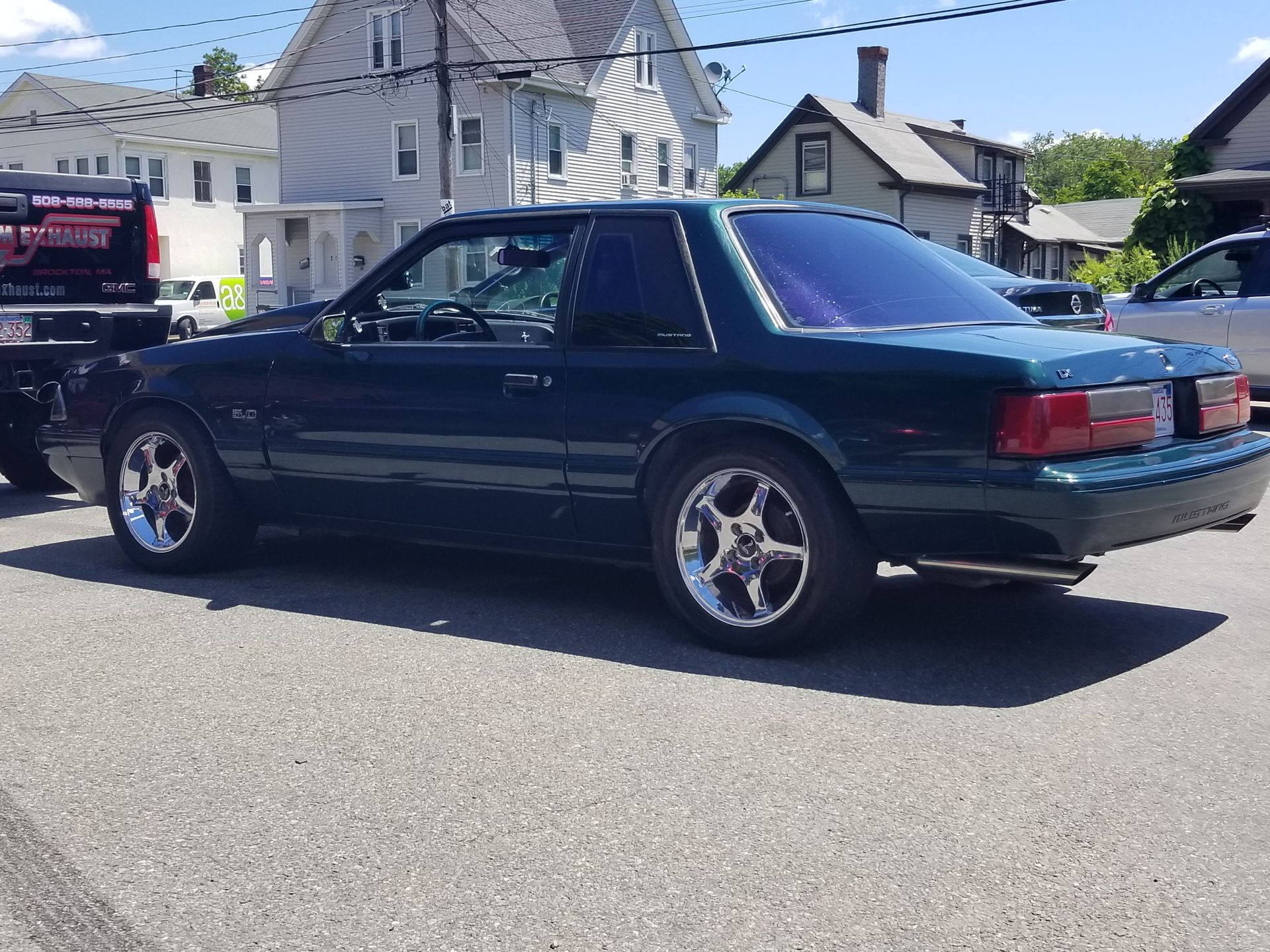 Dark green coupe parked on a sunny residential street with houses in the background