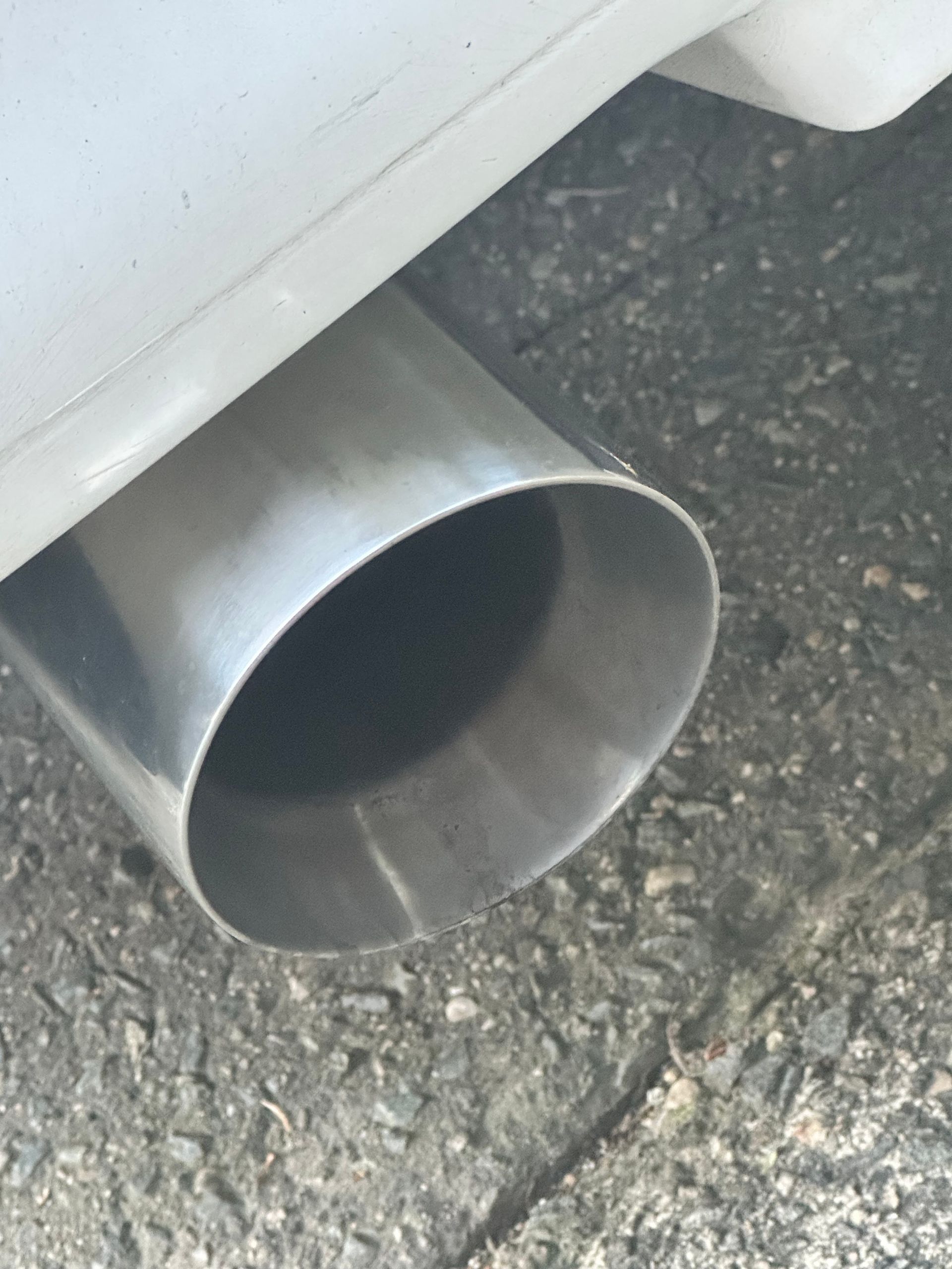Close-up of a car’s silver exhaust pipe extending over pavement.