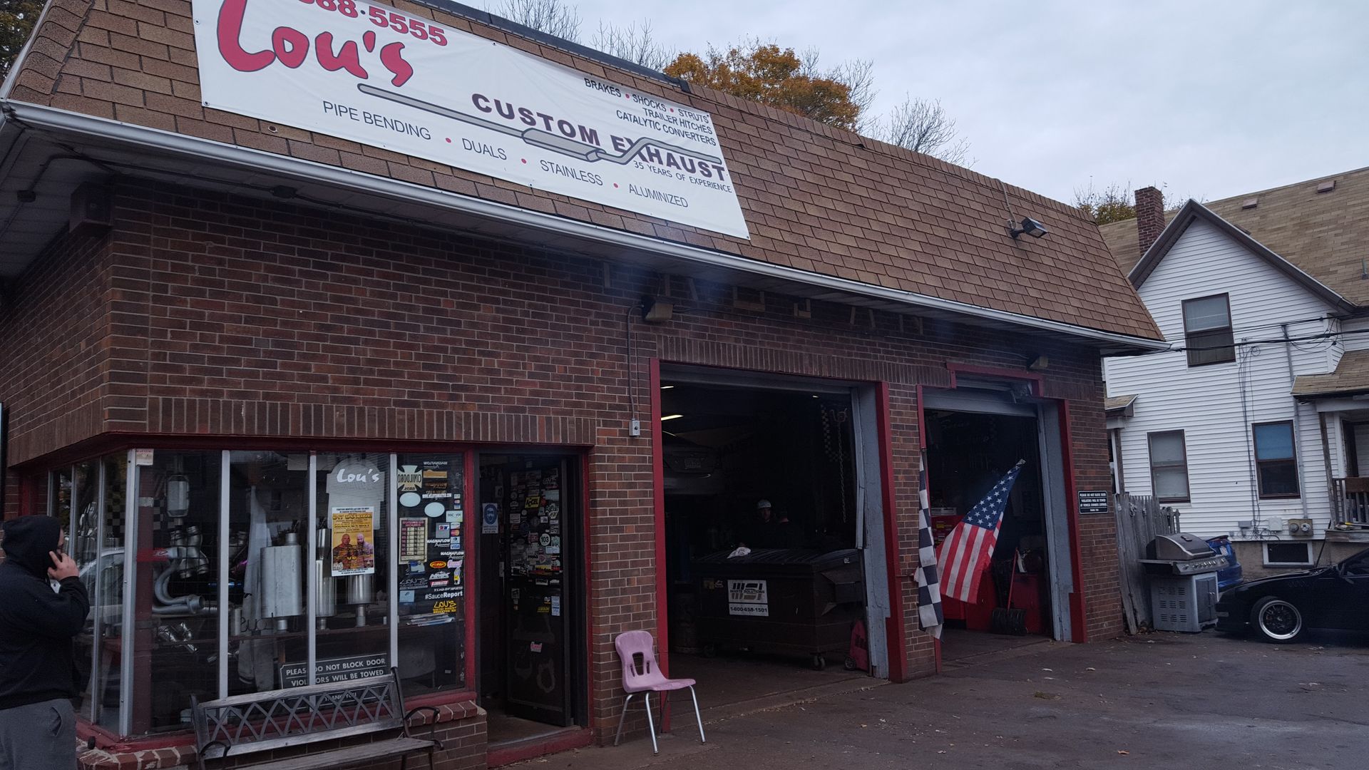 Brick storefront with red trim and open garage-style door, likely a shop, on a street corner.