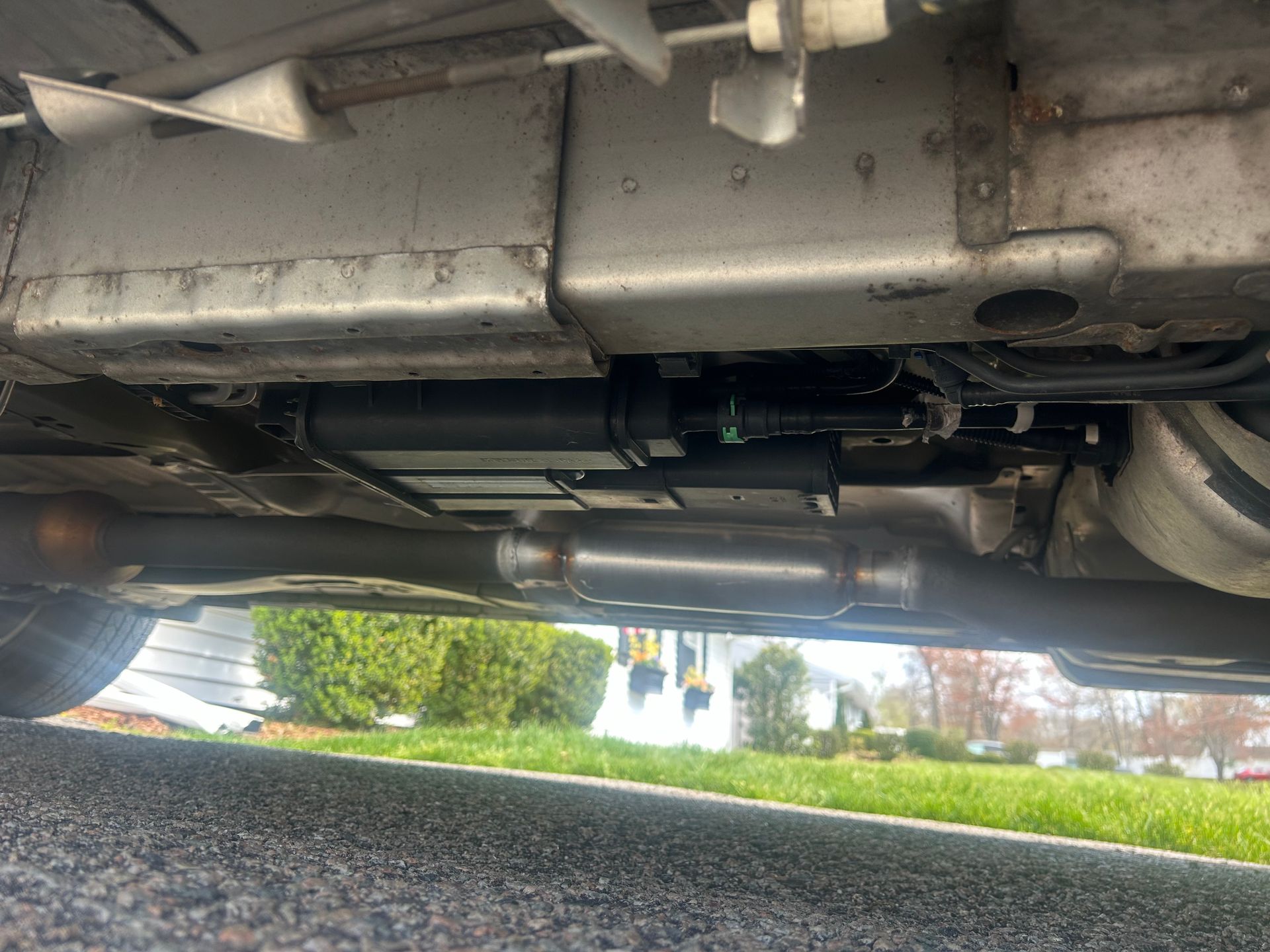 Undercarriage of a vehicle parked on a driveway, showing exhaust and suspension components.
