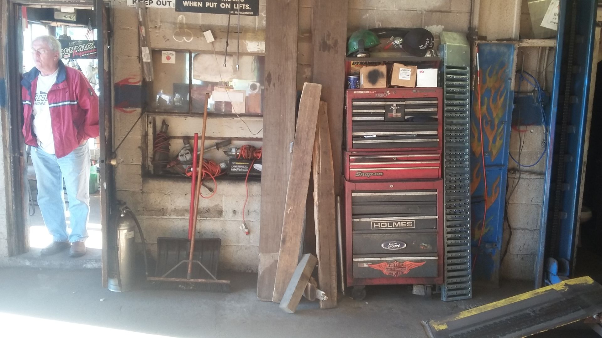 Garage workshop with shelves, a red tool chest, and a person standing in the doorway.