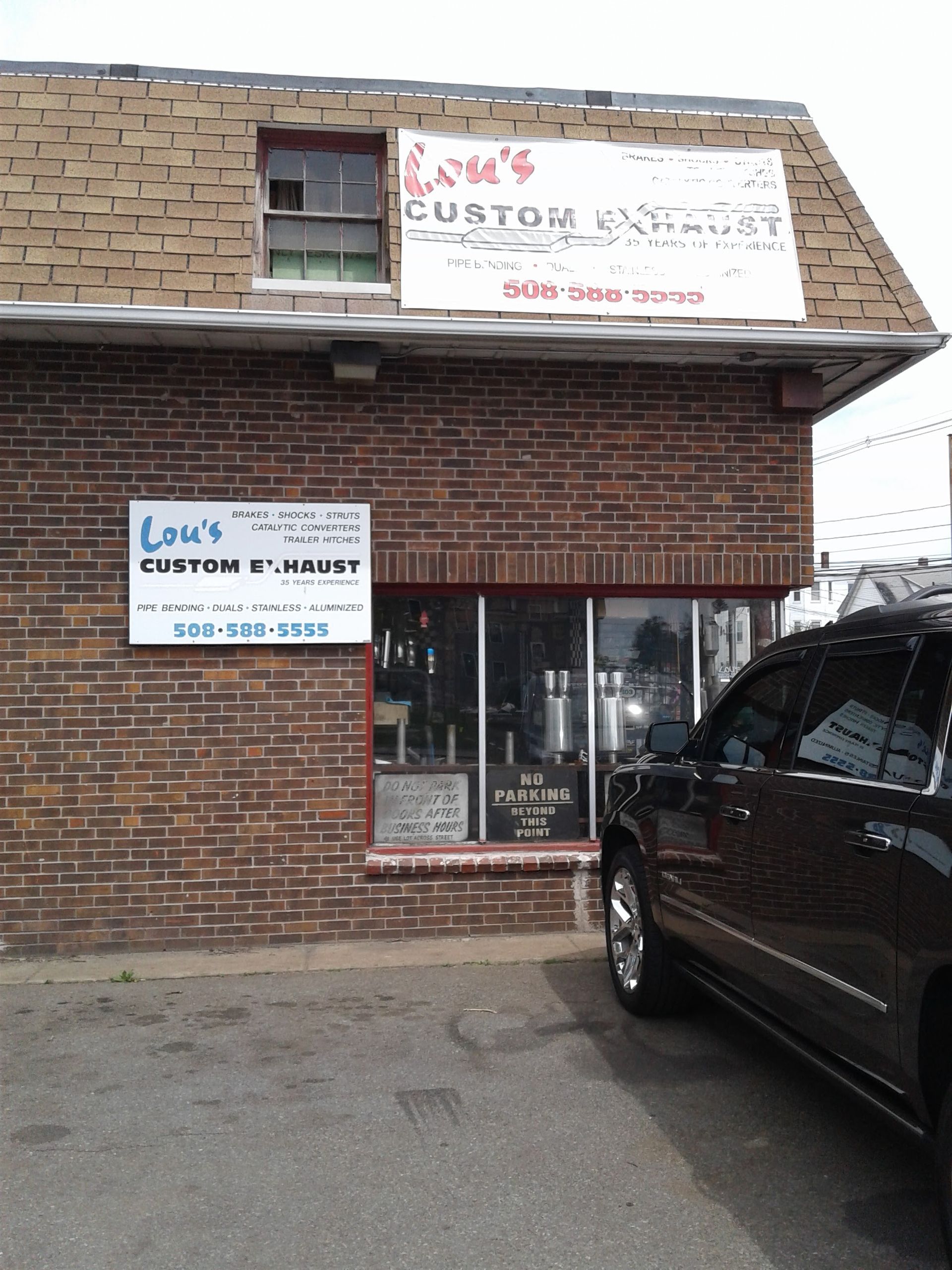 Brick storefront with signs, a small window, and a black SUV parked at the entrance.