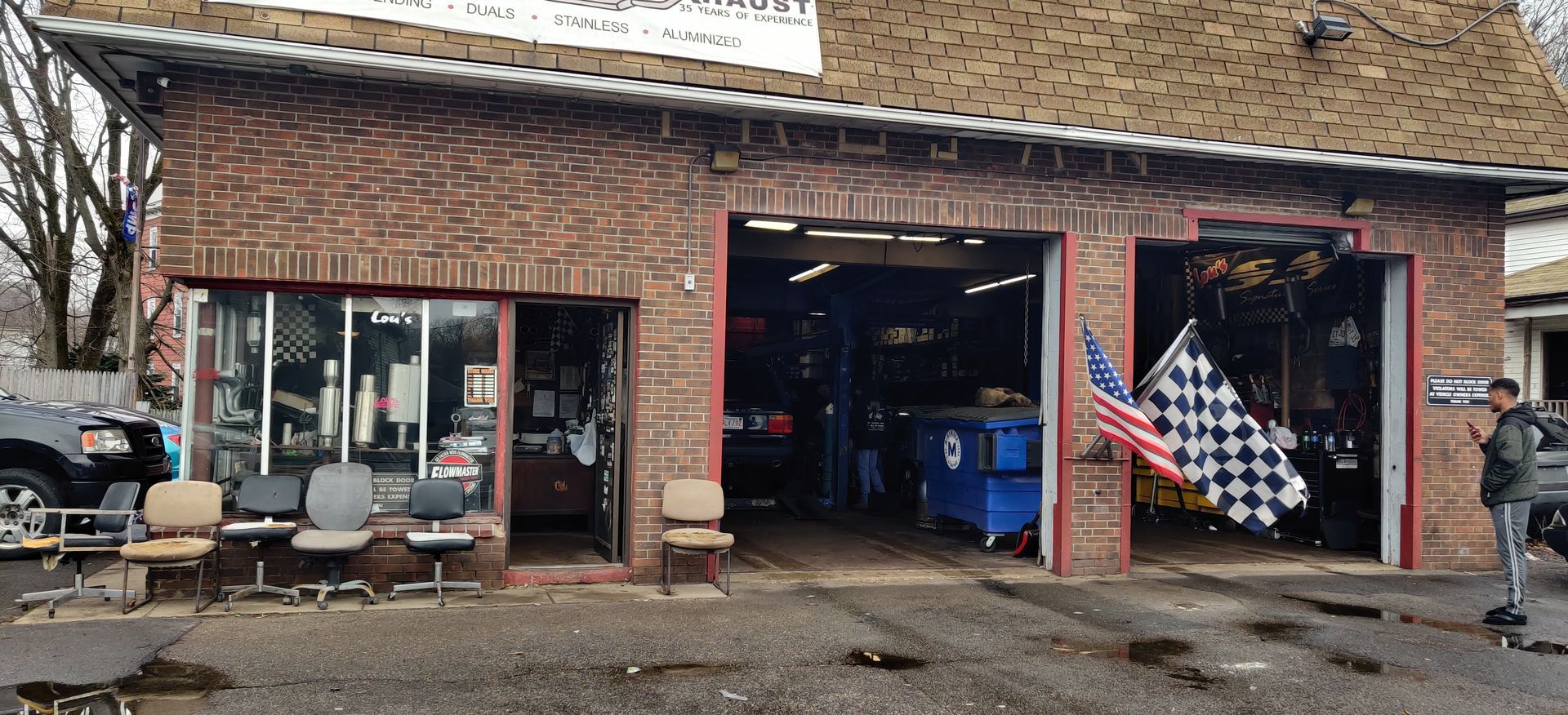 Small brick storefront with an open garage door, display windows, and a checkered flag on a rainy street.