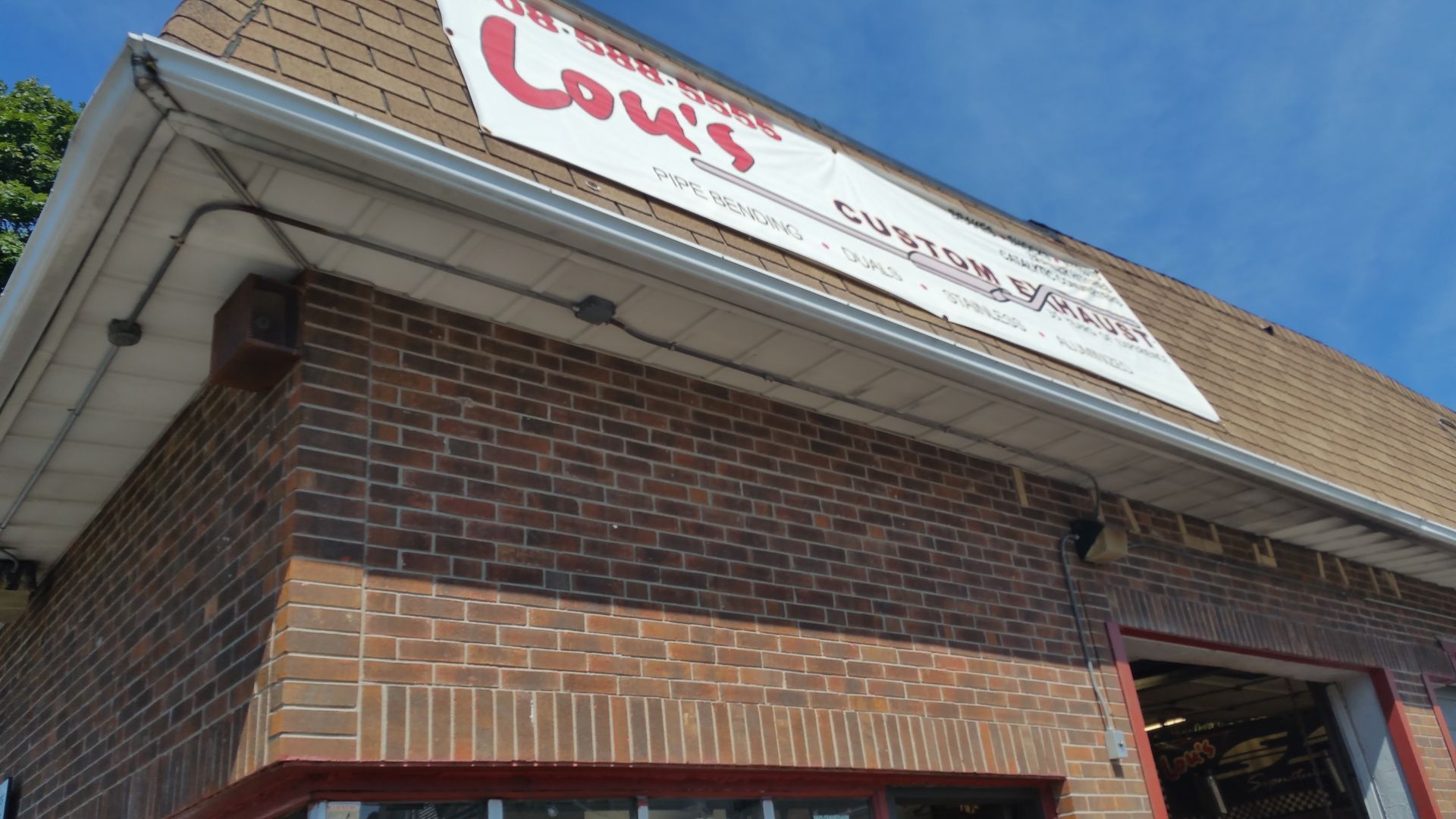 Brick storefront with a white-and-red sign under a blue sky, viewed from below