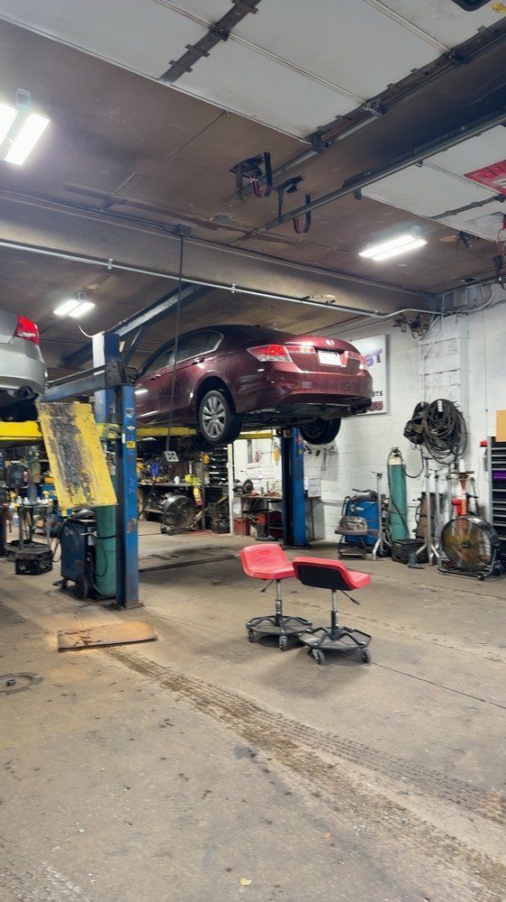 Red car lifted on a mechanic’s hoist inside an auto repair shop with tools and chairs nearby