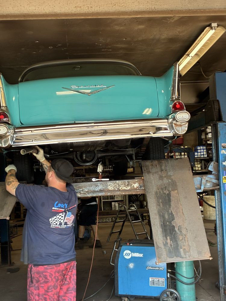 Mechanic working under a turquoise classic car on a lift in a garage