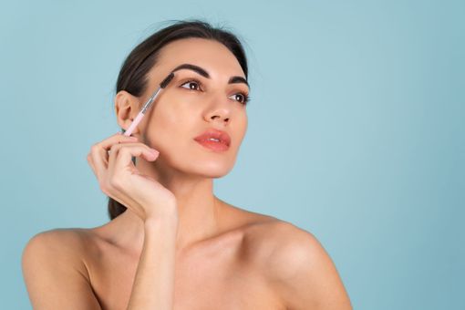 A woman is applying eyebrow pencil to her eyebrows.
