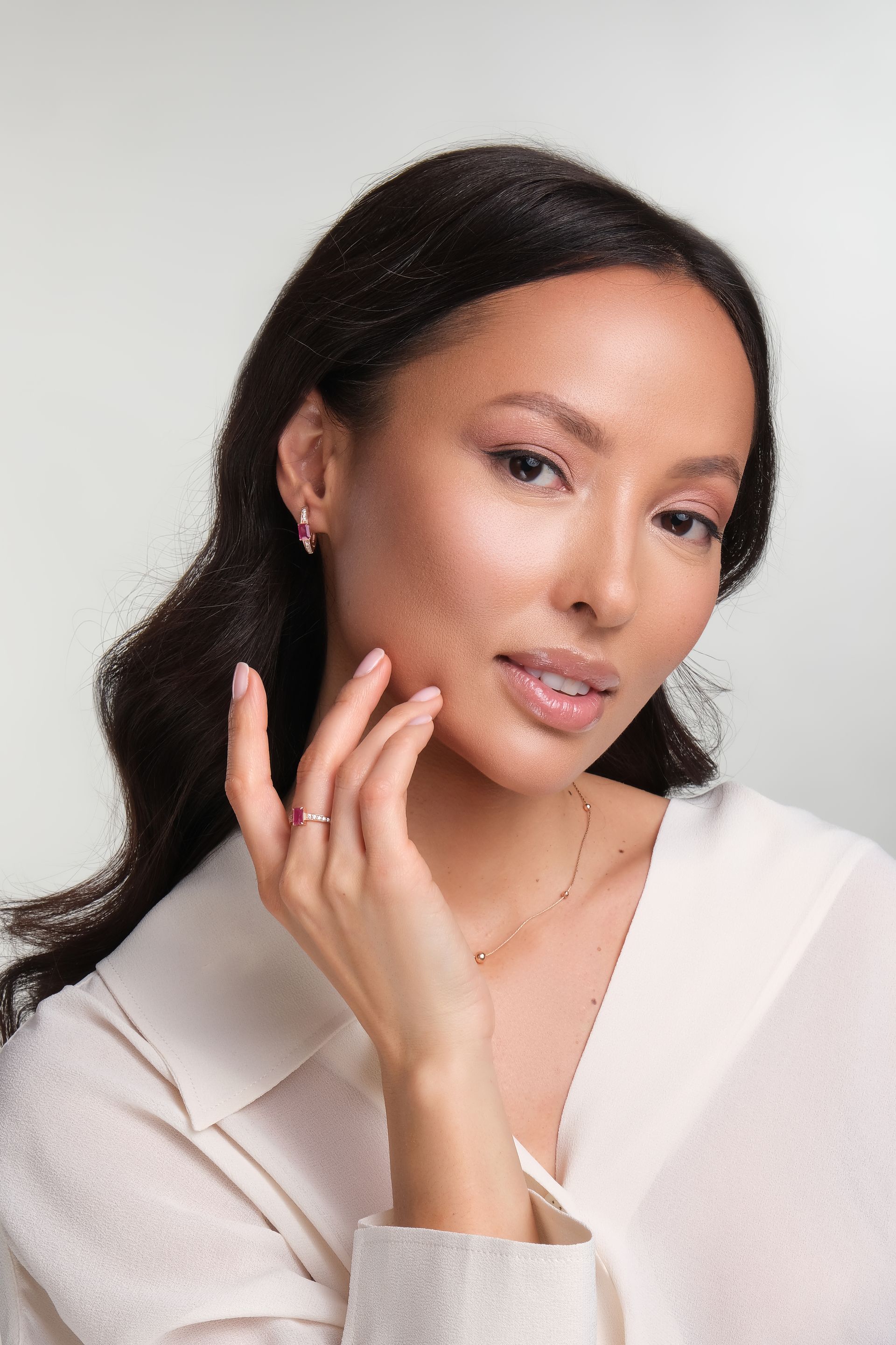 A woman wearing a white shirt and earrings is touching her face.