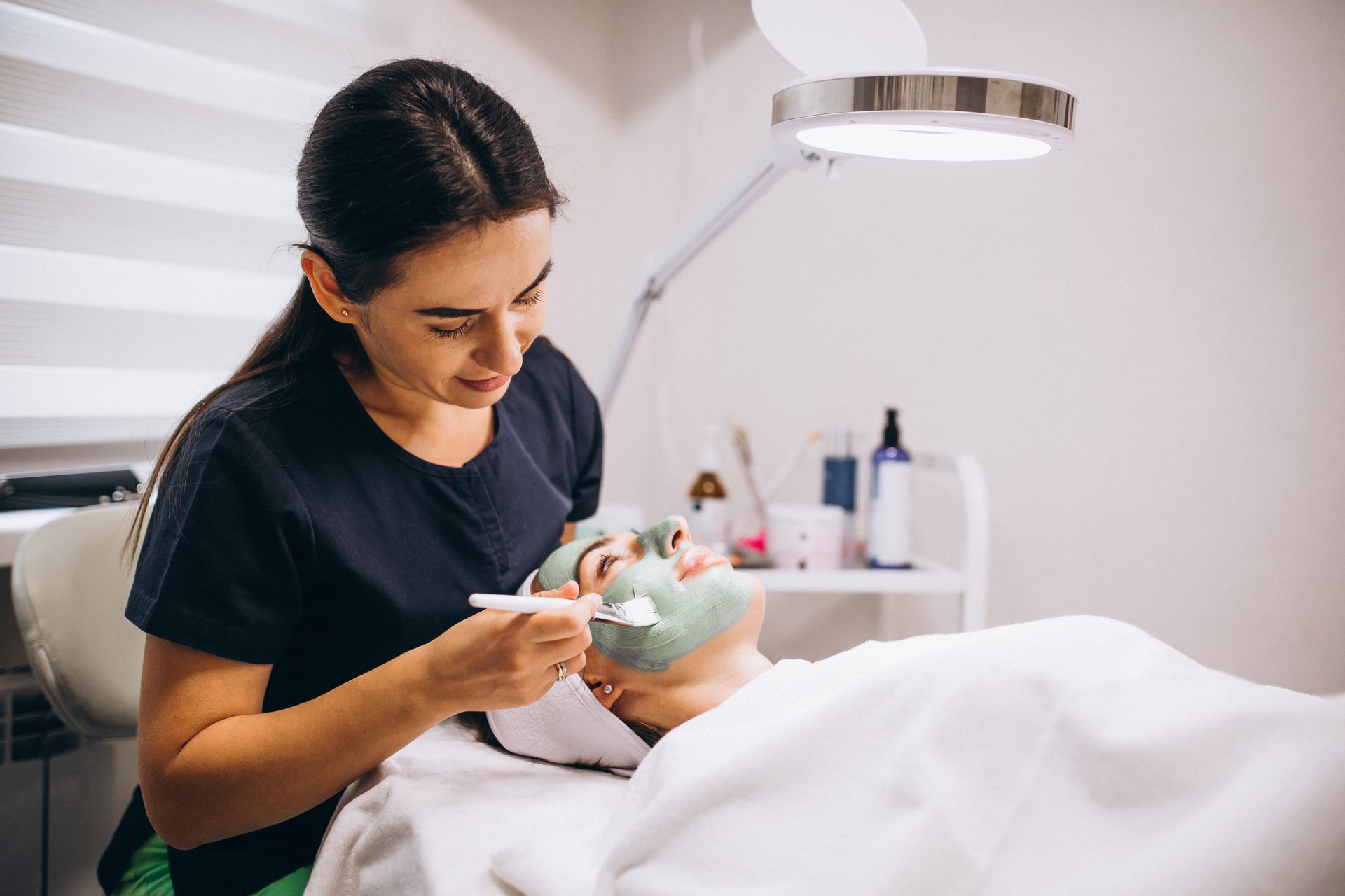A woman is applying a green mask to a woman 's face in a beauty salon.