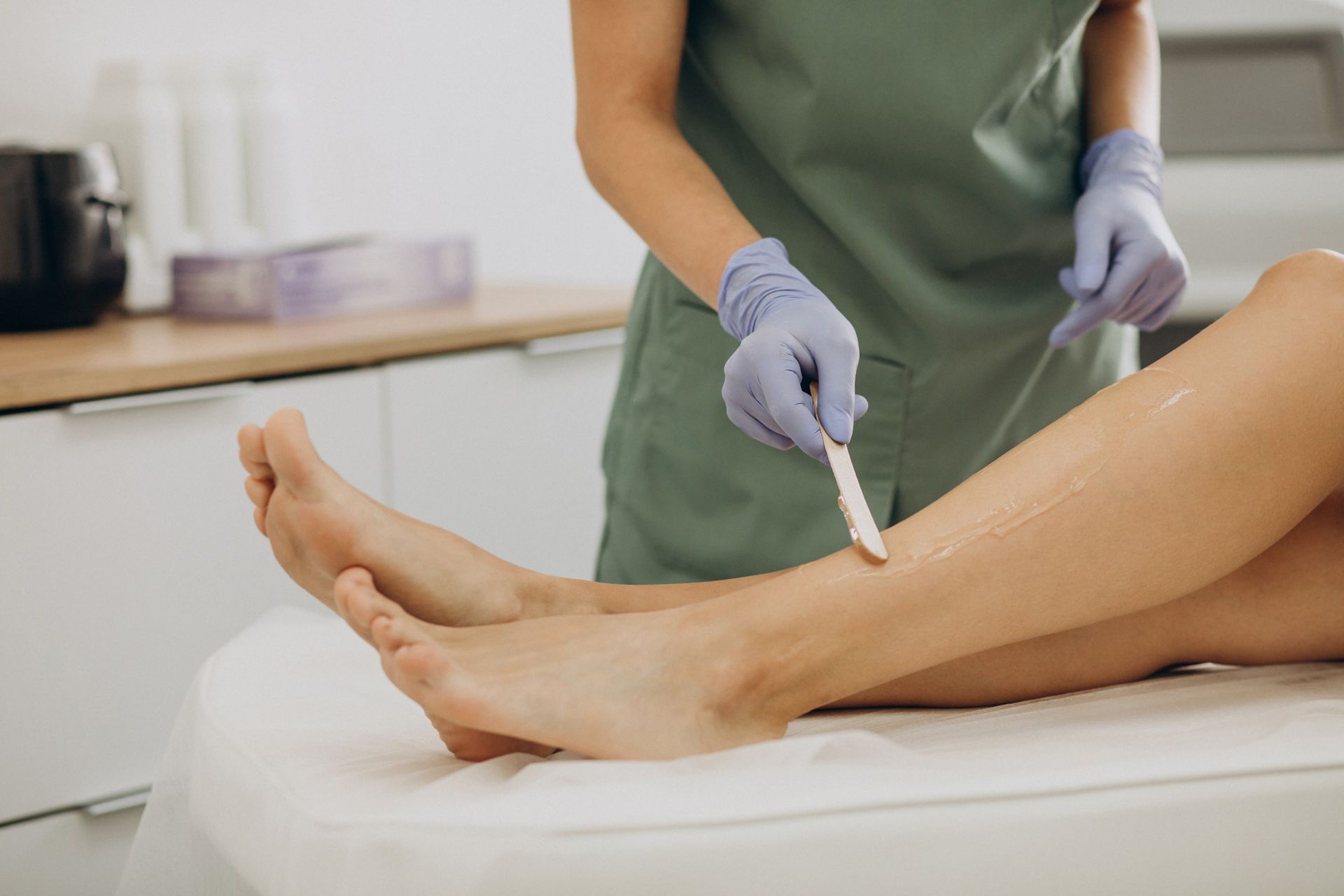 Person applying wax to leg on a table in a salon, using a spatula.