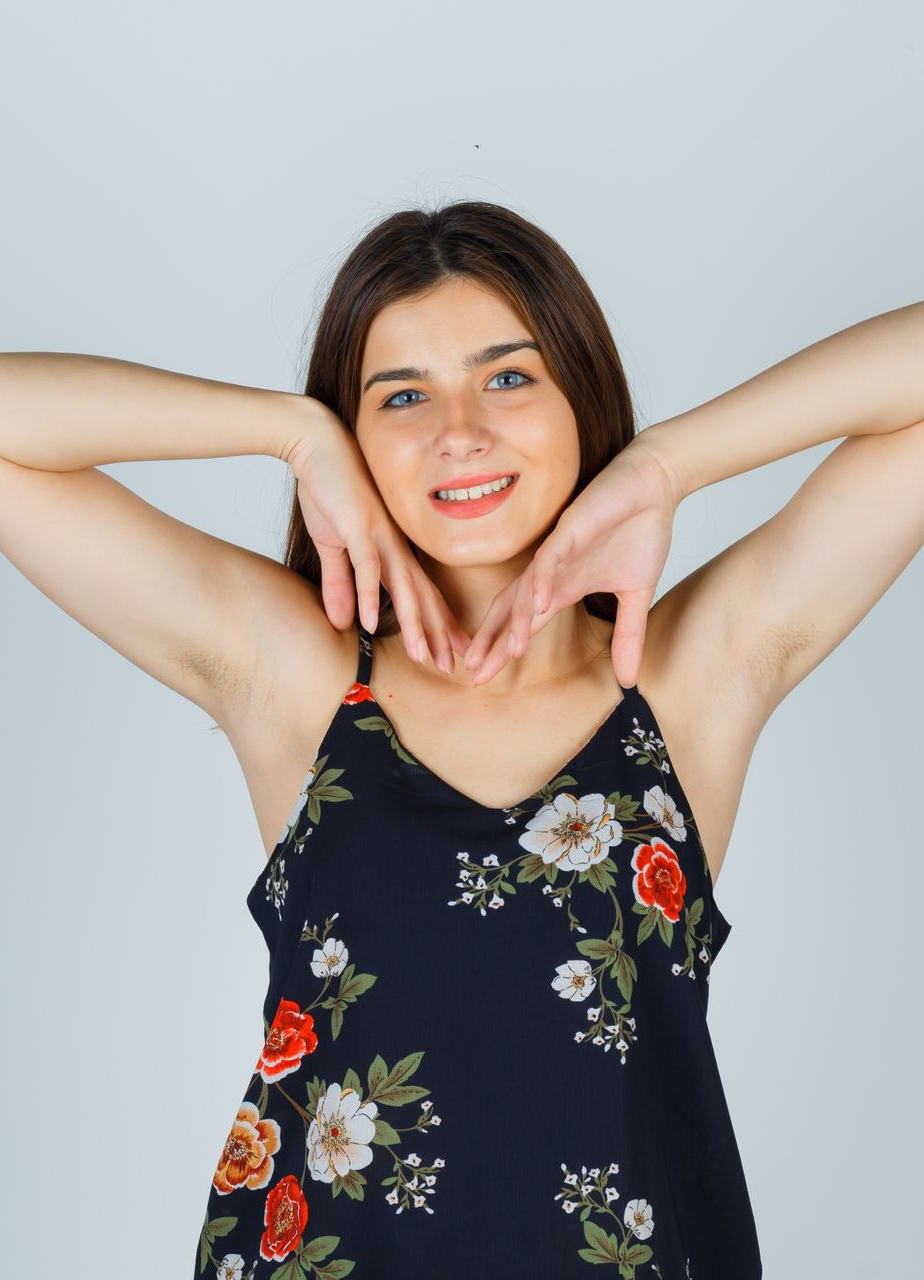 Woman in floral top smiles, holding hands near face.