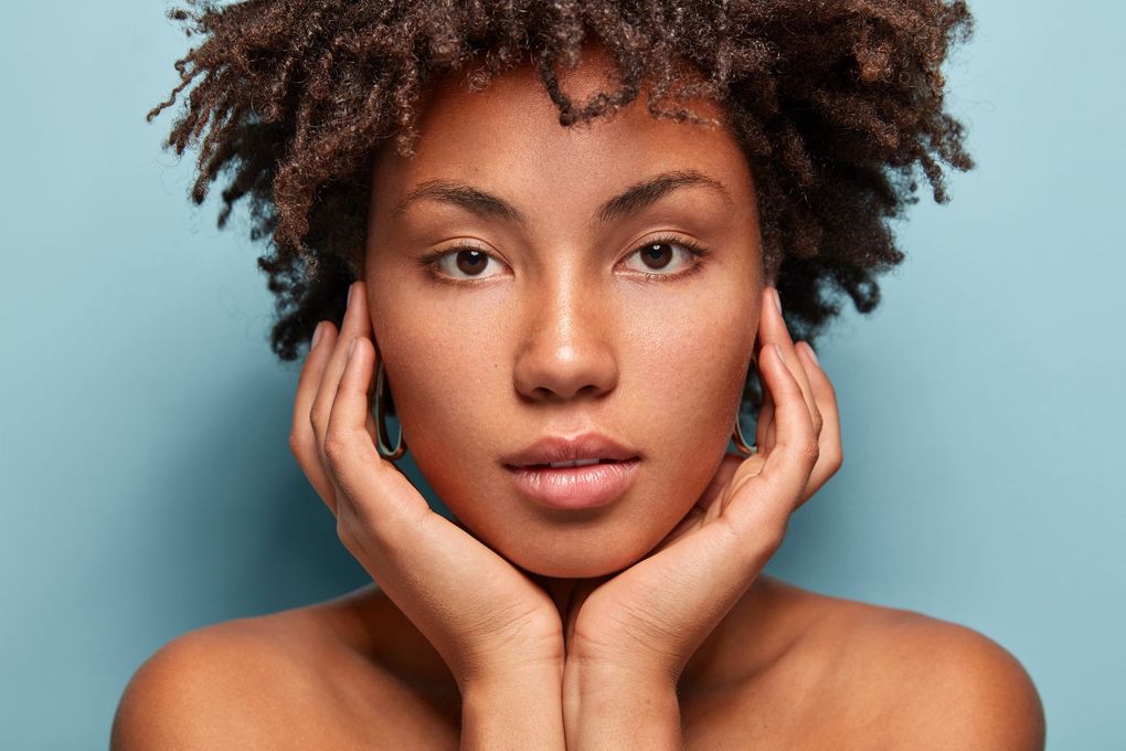 A woman with curly hair is holding her face with her hands.