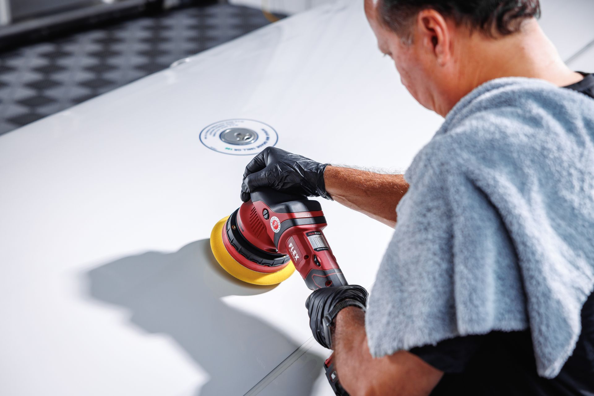 A man is polishing a white car with a machine.