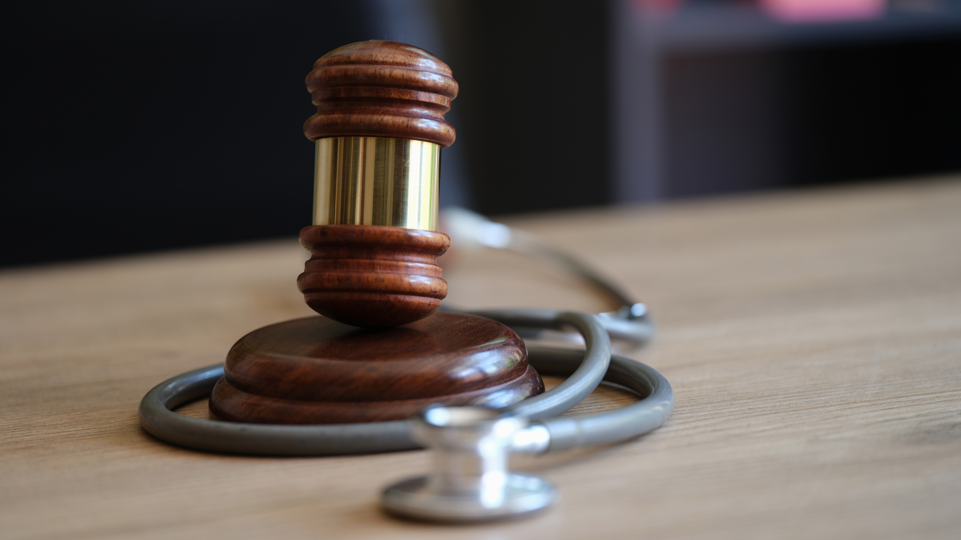 A judge 's gavel is sitting on top of a stethoscope on a wooden table.