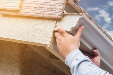 Hands installing white soffit panels beneath a house roof edge