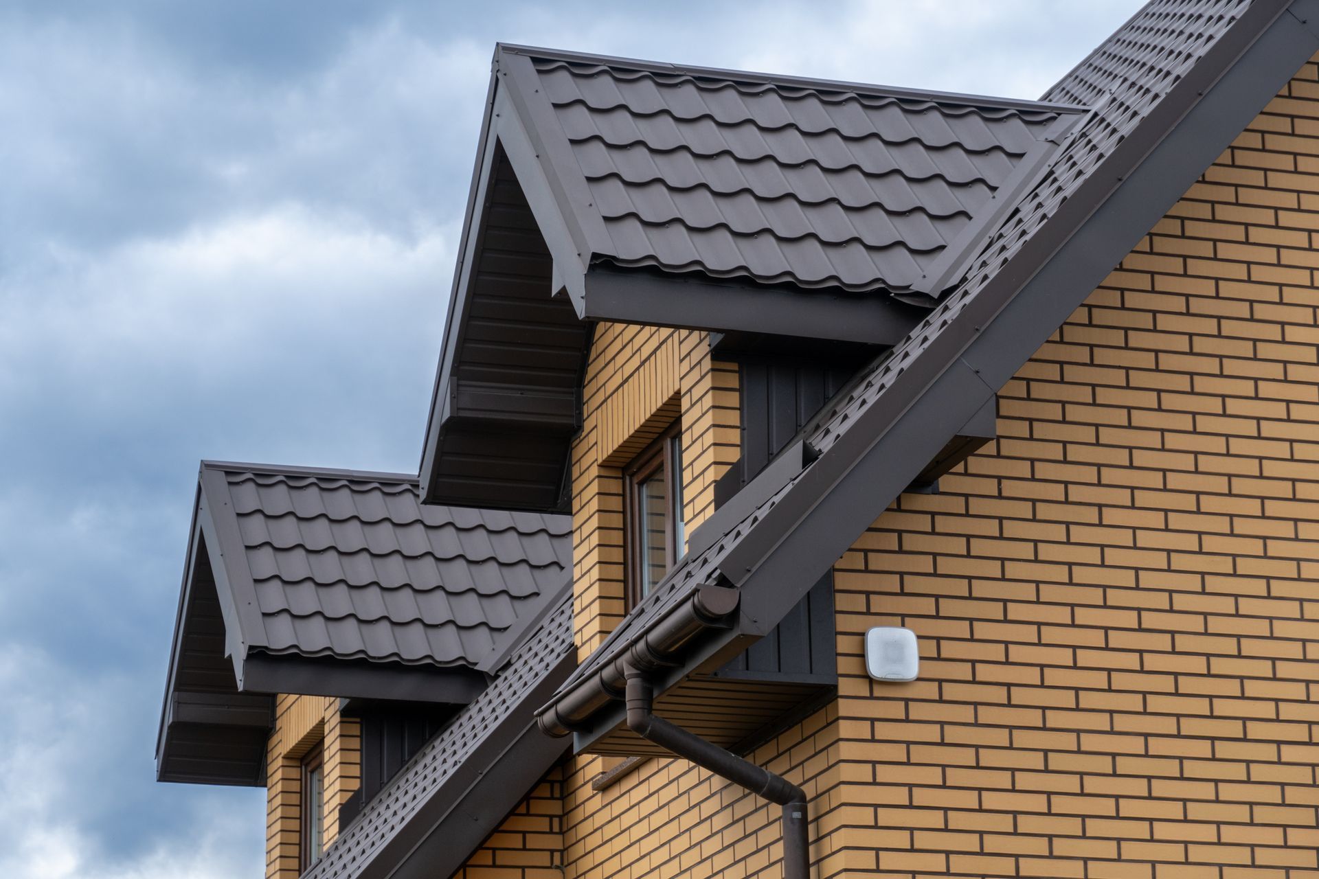 Close-up of a brick house with dark gray gabled roof under a cloudy sky